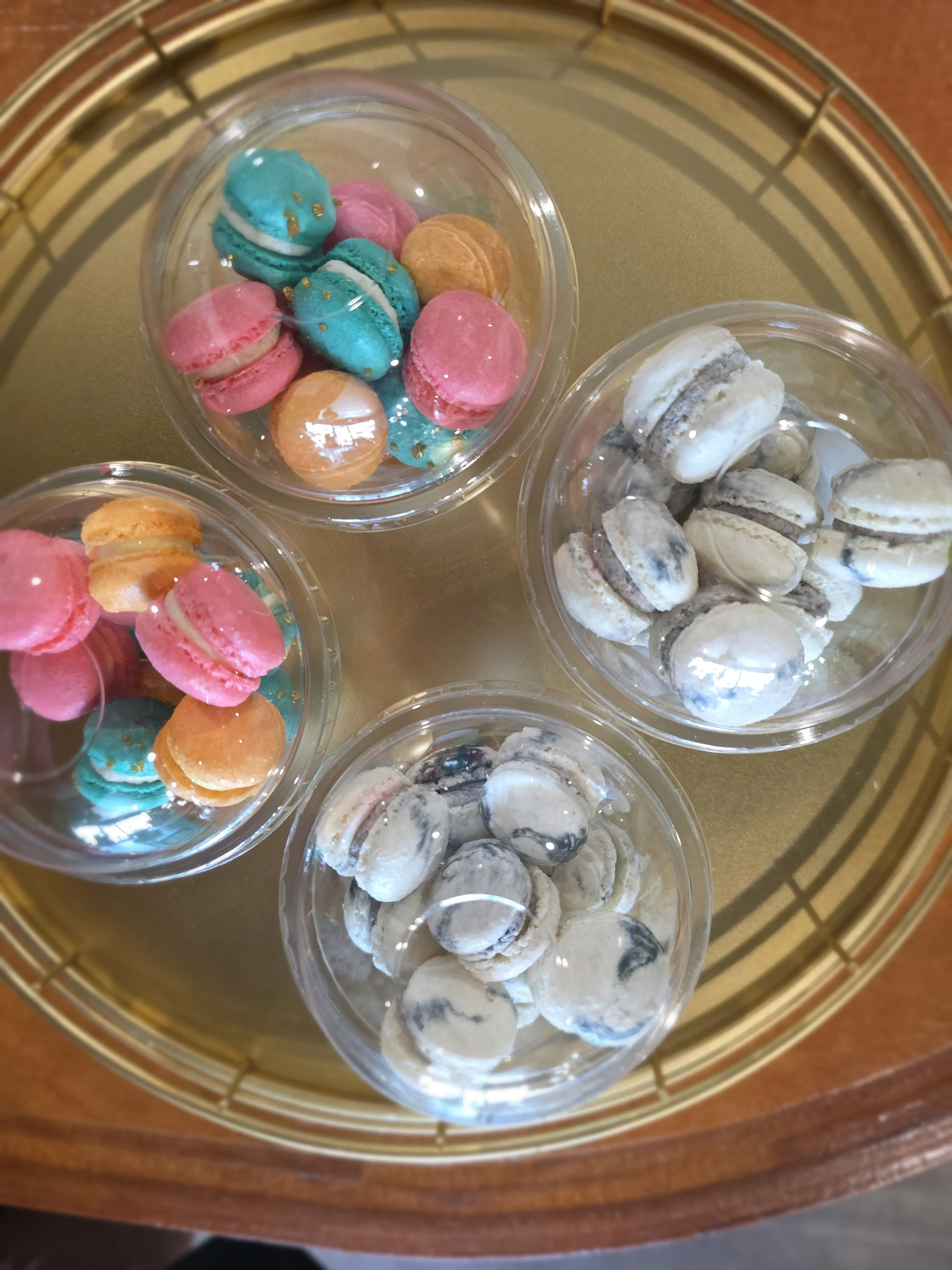 Multiple bowls of macarons in different colors, including pink, blue, orange, and white, organized inside a round woven basket or tray.