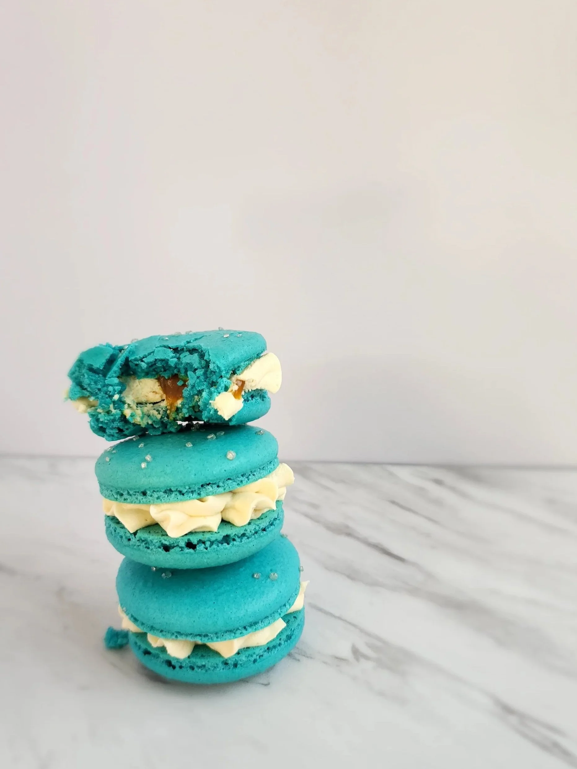 Stack of four blue macarons with cream filling on a marble surface.