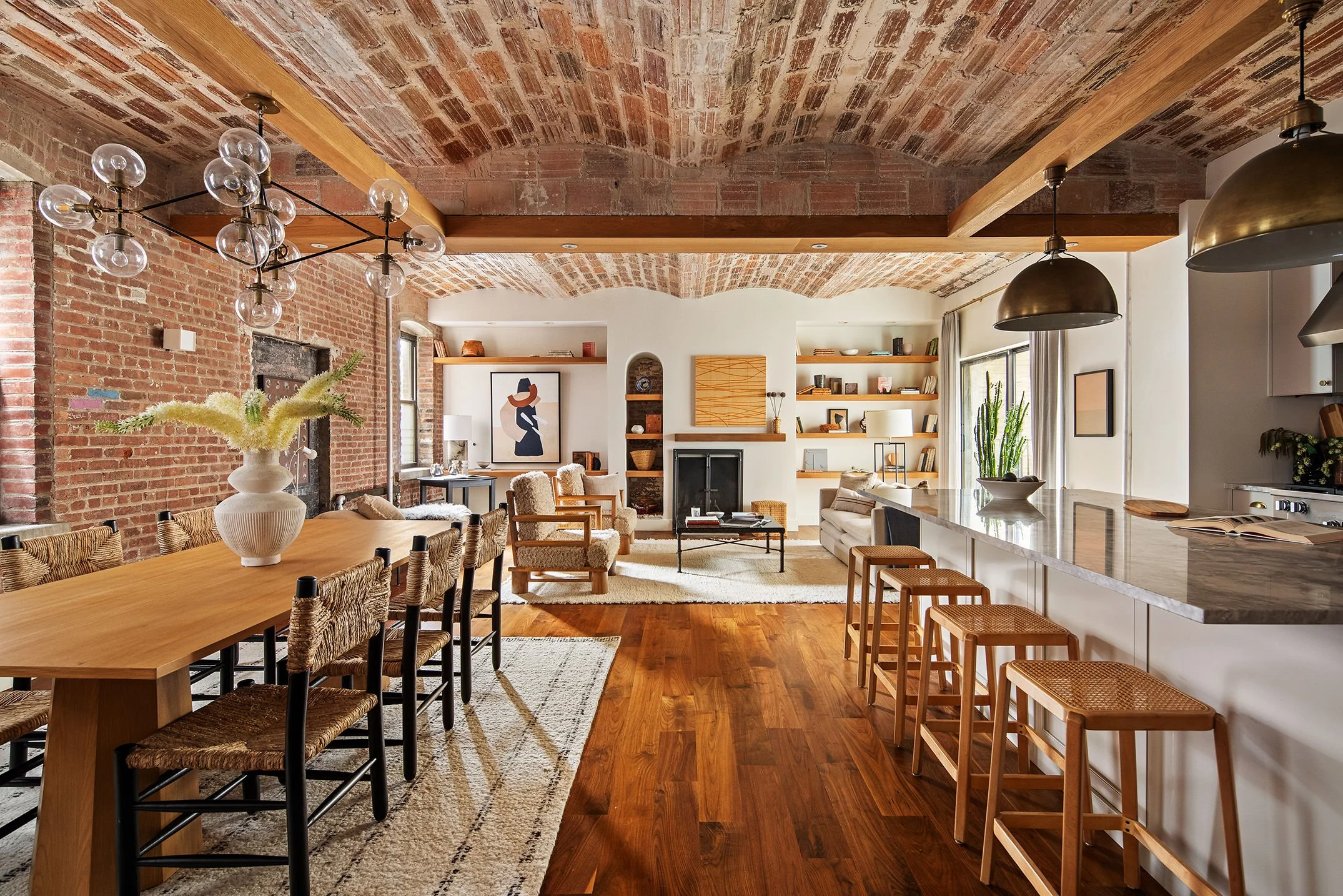  view of living room from dining room, on the left a dining table is seen with a chandelier, on the right is a set of barstools arranged at a white marble kitchen island 