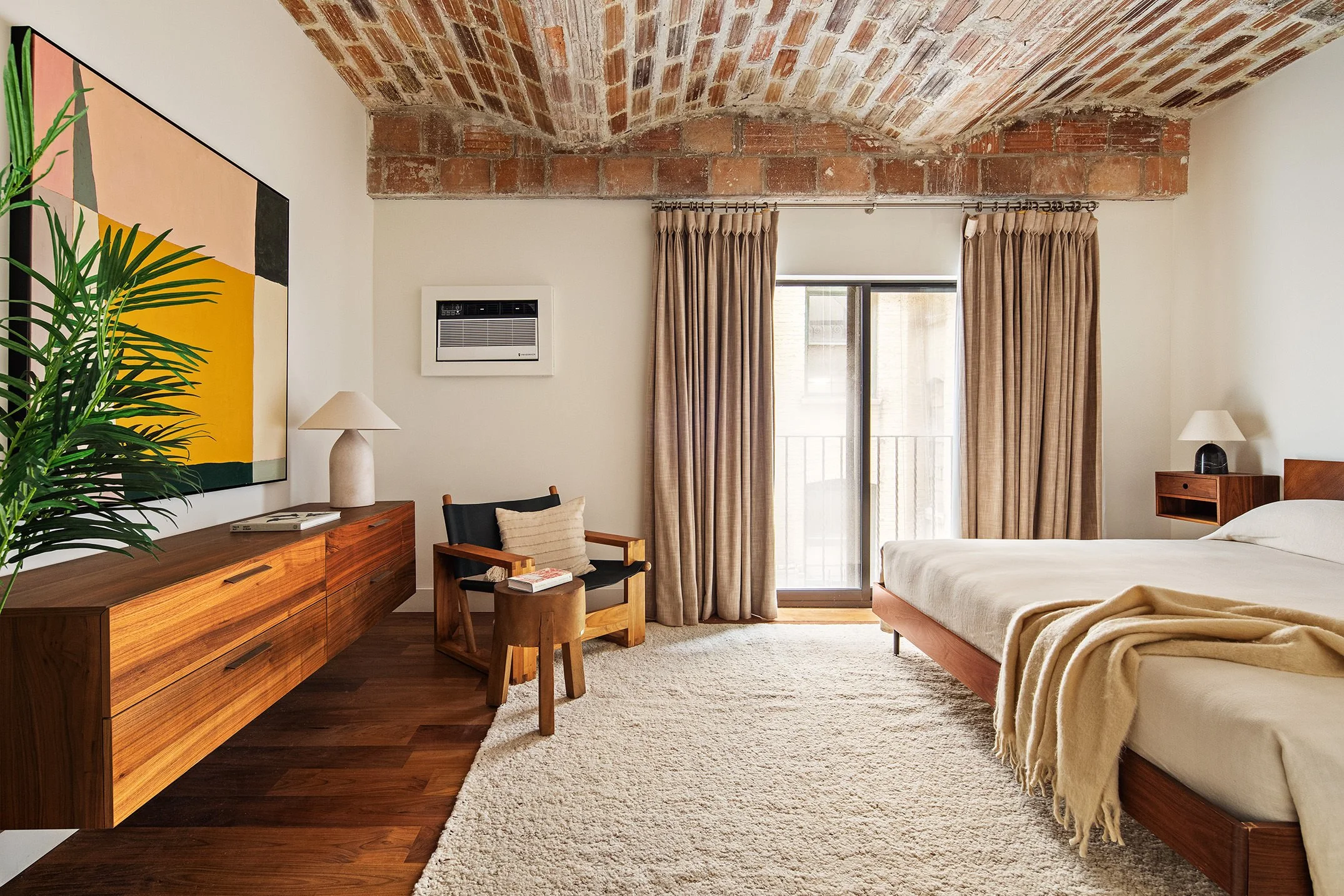  warm toned bedroom with a white rug and white bedding, a brick ceiling accents warm wooded floors and a floating dresser 