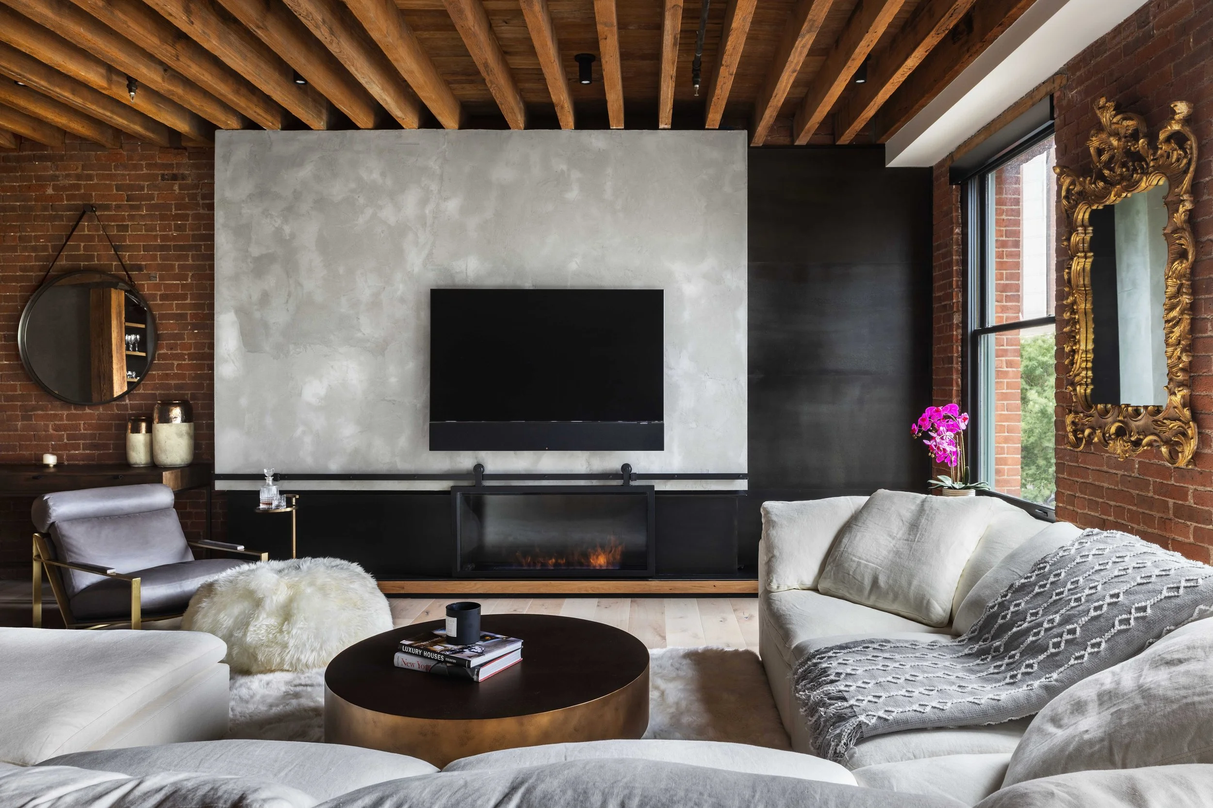  living room view facing tv and fireplace with whitewashed accent wall, brick, and exposed beams 