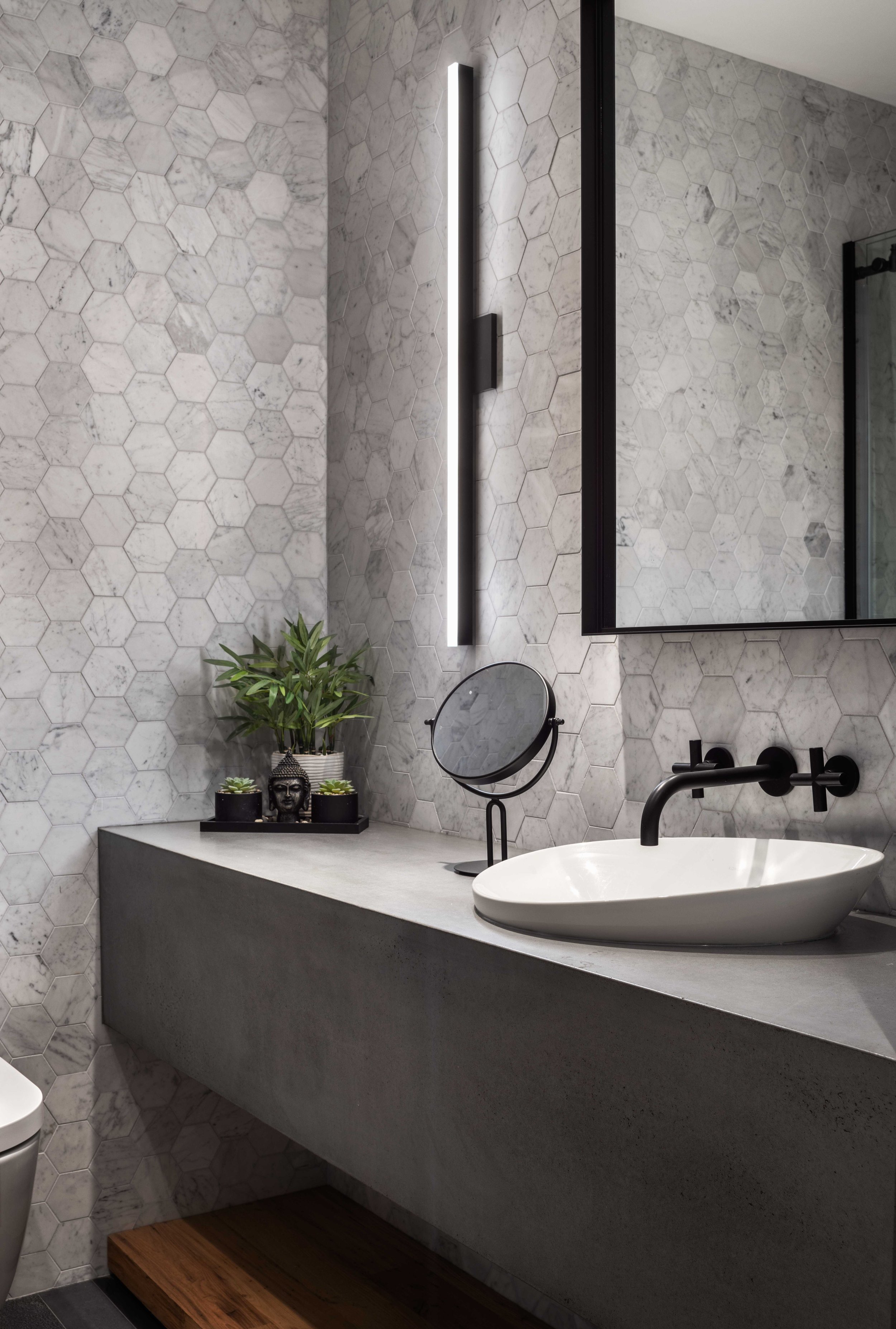  sink in bathroom on concrete countertop with grey tiled walls and warm lighting 