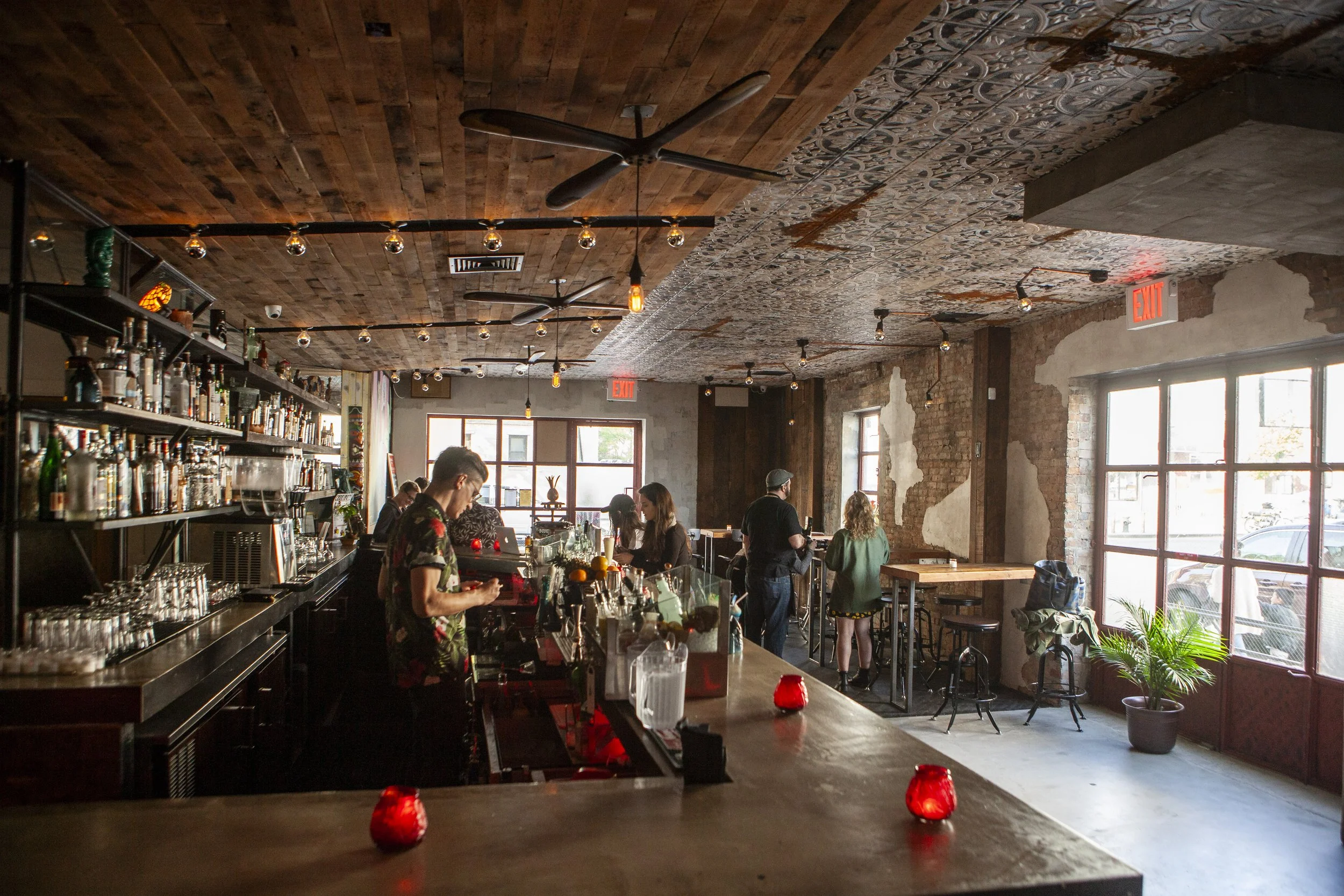  view of restaurant bar from the side view, shelves of liquors to the left and patrons across bar to the right looking at menus 