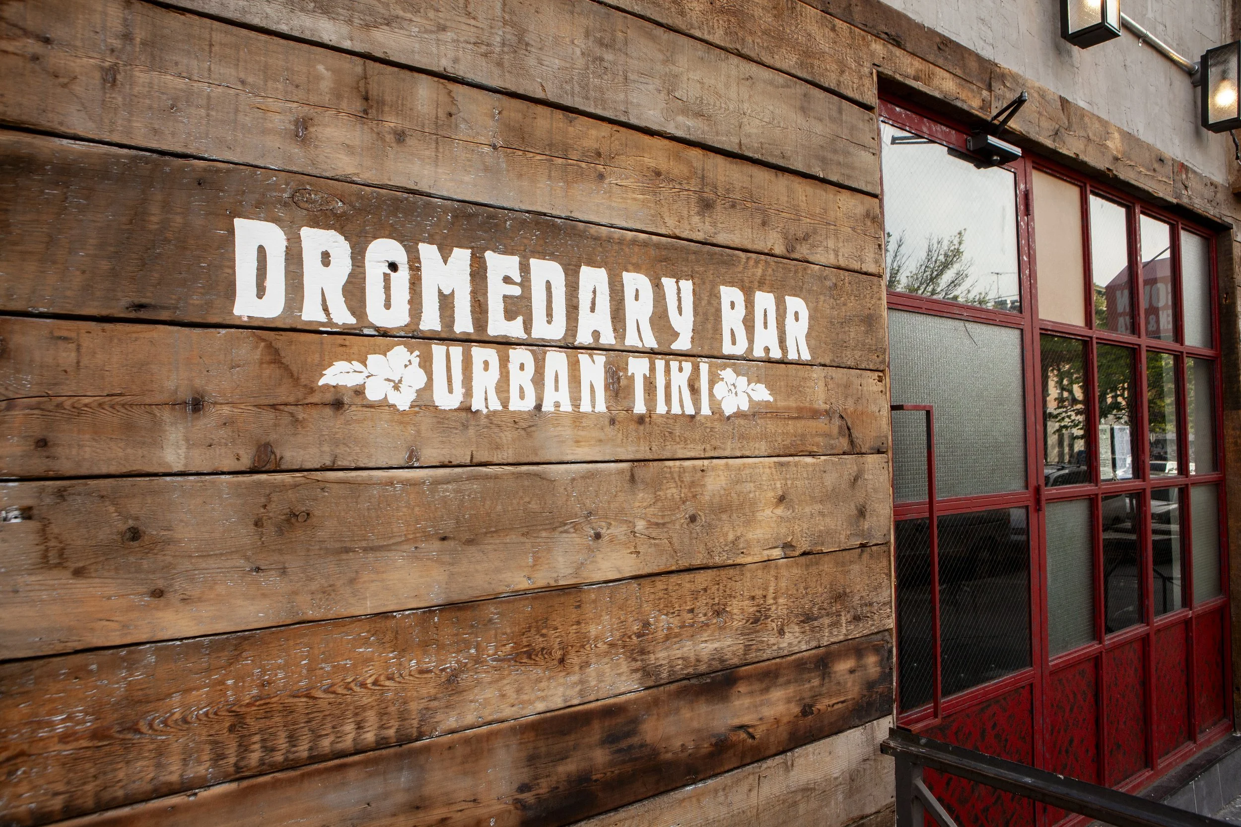  white sign on wooden paneling that says dromedary bar, urban tiki 