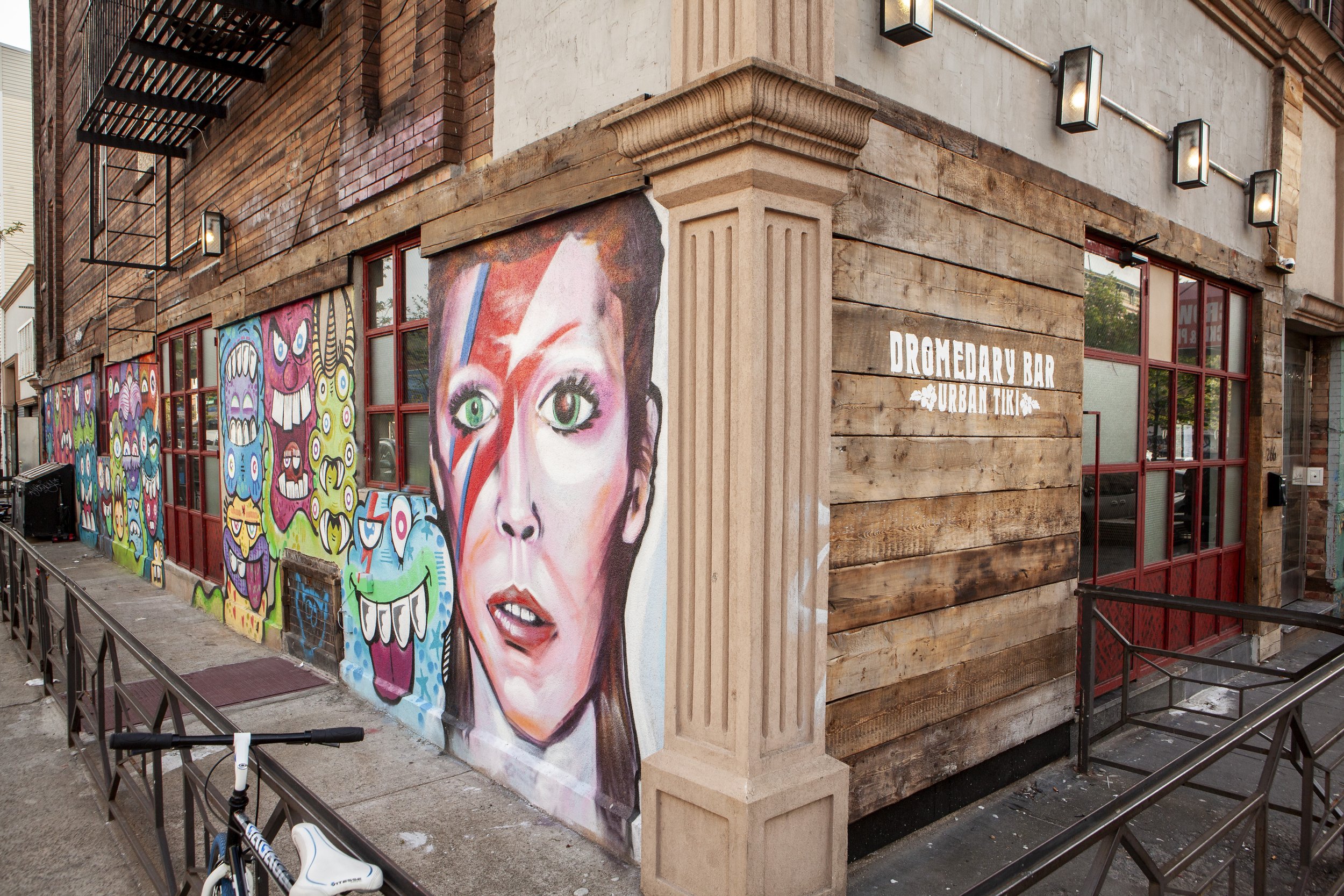  exterior view of tiki bar with wall covered in murals including one of david bowie 