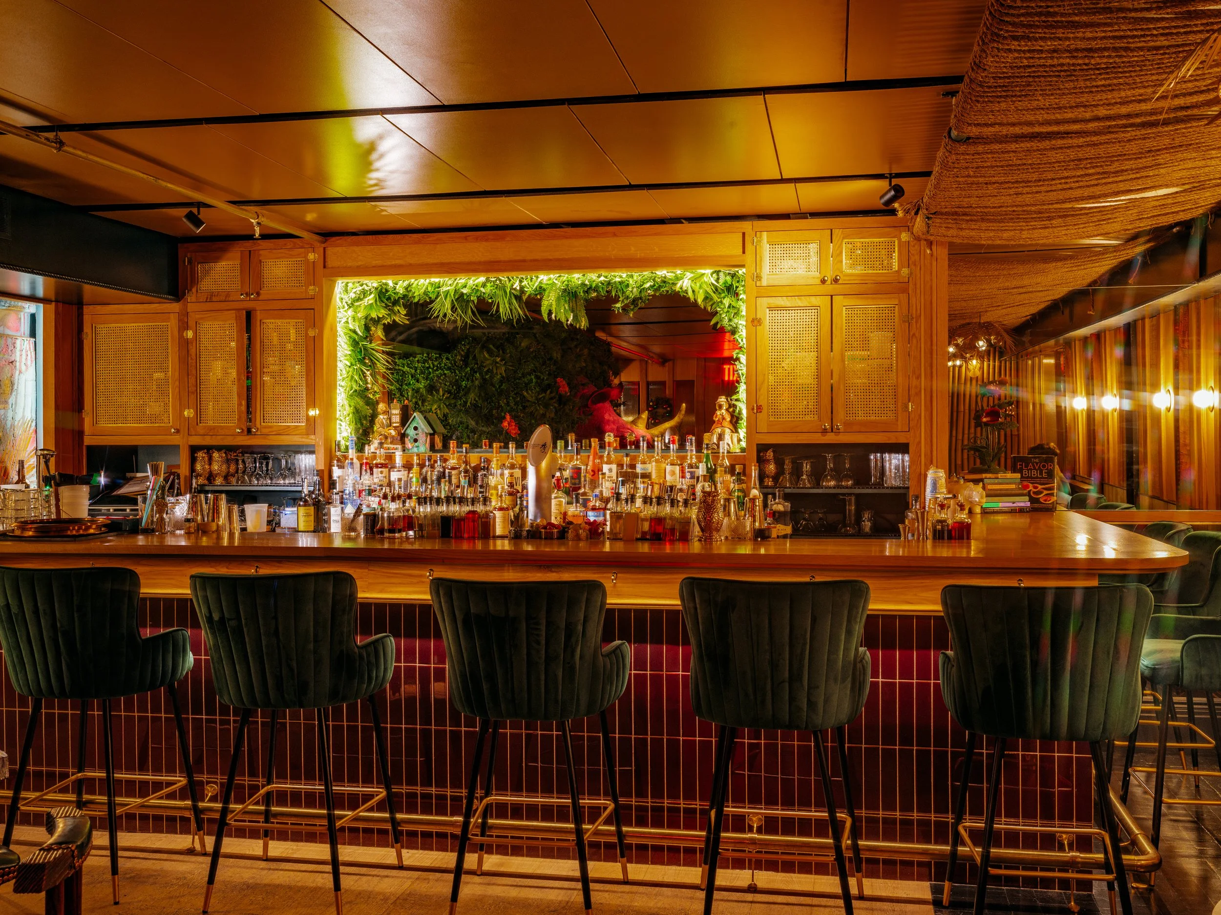  teal velvet barstools lined up against maroon tiled bar with wooden bartop and mirror surrounded by leaf accents 