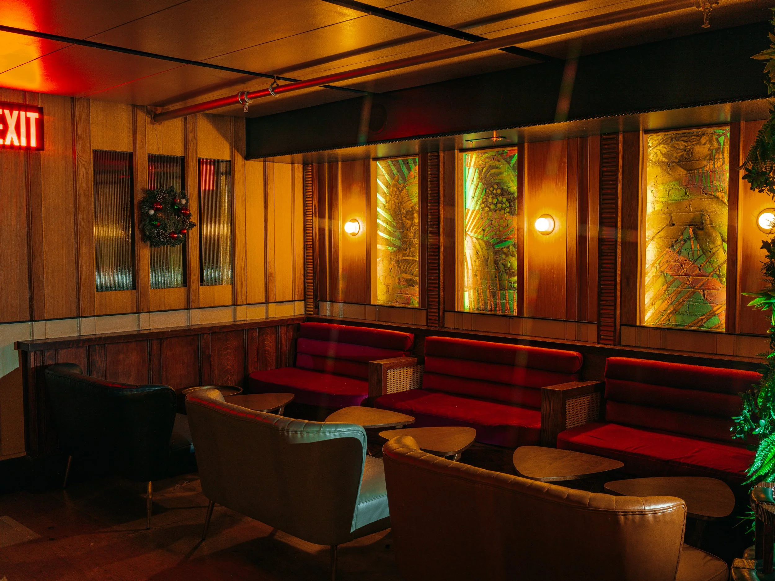  sitting area in restaurant with warm yellow lighting and six couches all arranged to face each other, some couches are red with black straps and some are teal 