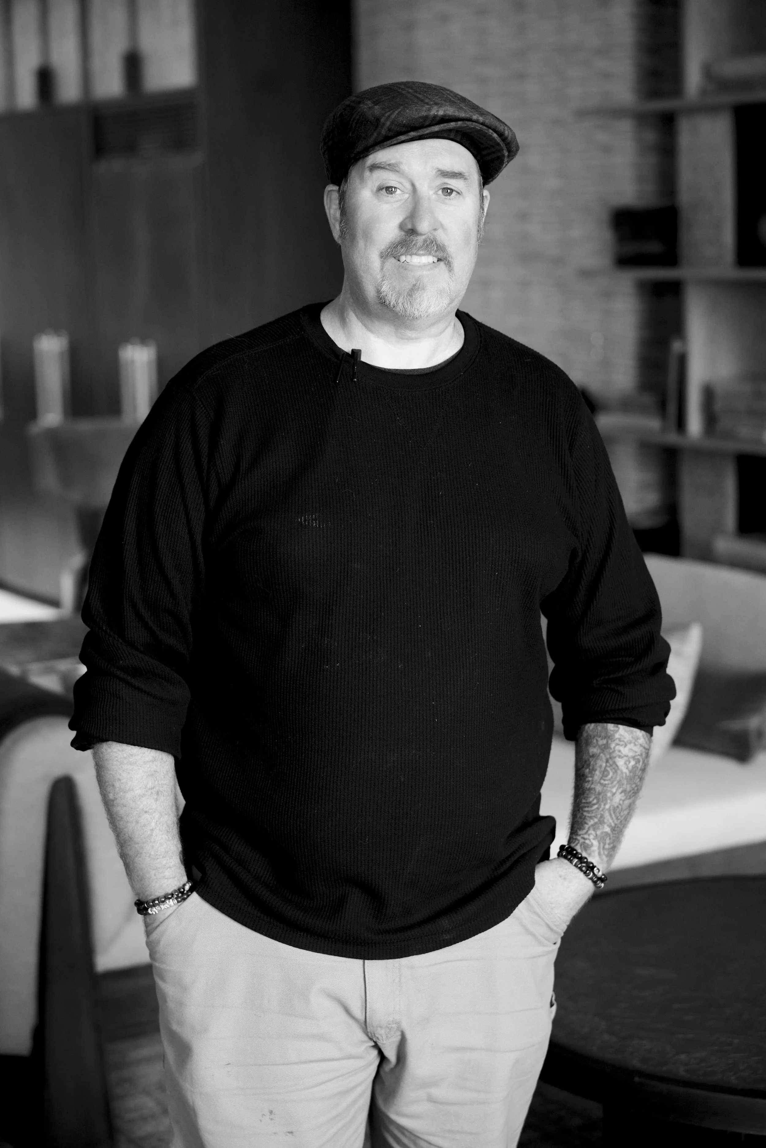 A man with tattoos and light facial hair with a paper boy hat and black longsleeve
