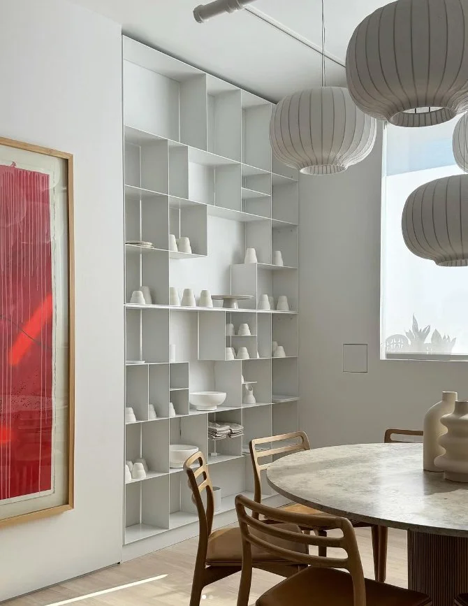 View of monochromatic white shelves in modern residential dining room with a wooden table and accent art