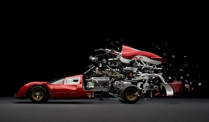 Une voiture de course Ferrari rouge en cours de démontage, avec des pièces mécaniques dispersées autour, sur fond noir.