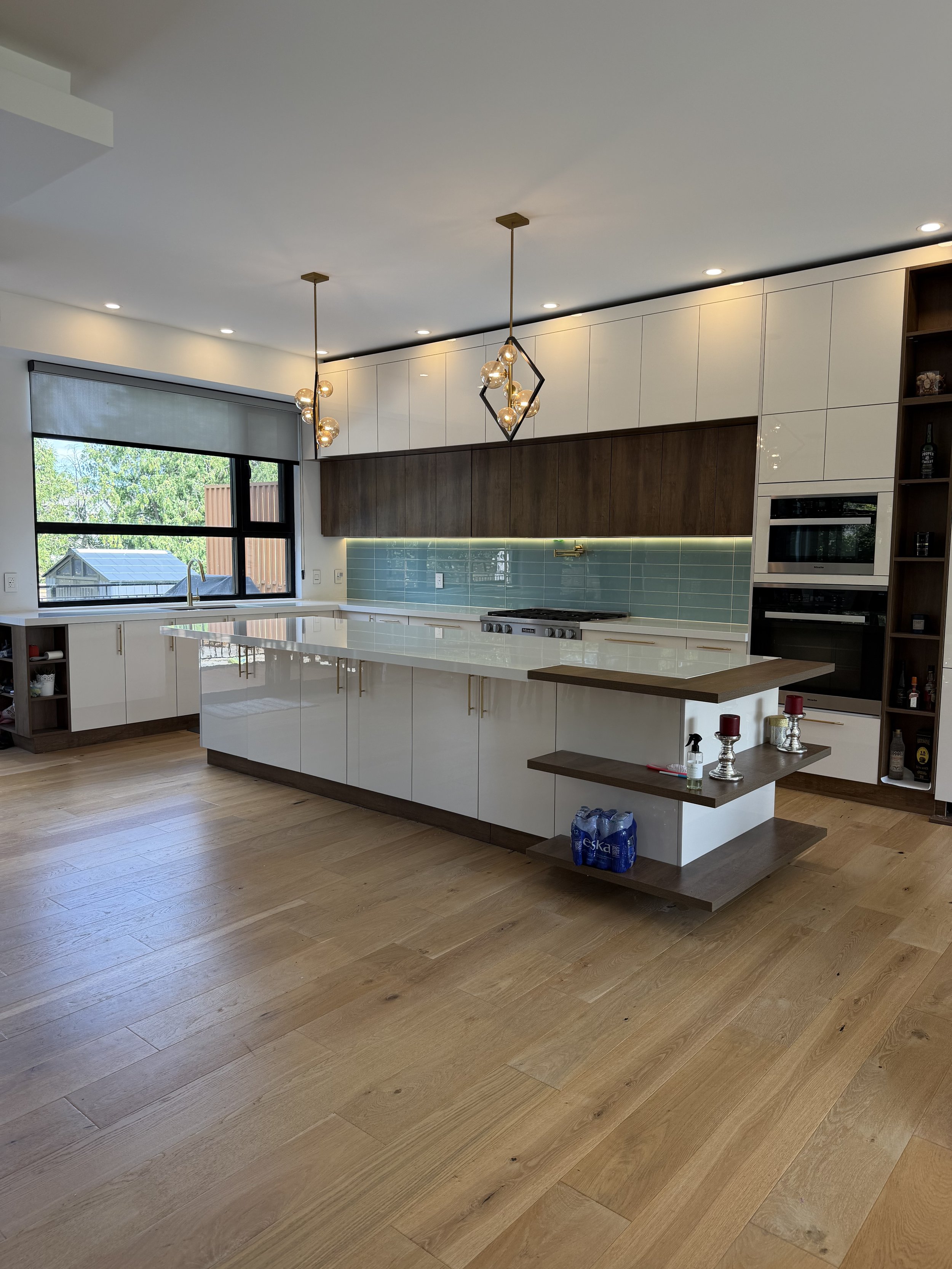 Modern kitchen with large window, white and wood cabinets, a kitchen island, and pendant lights.