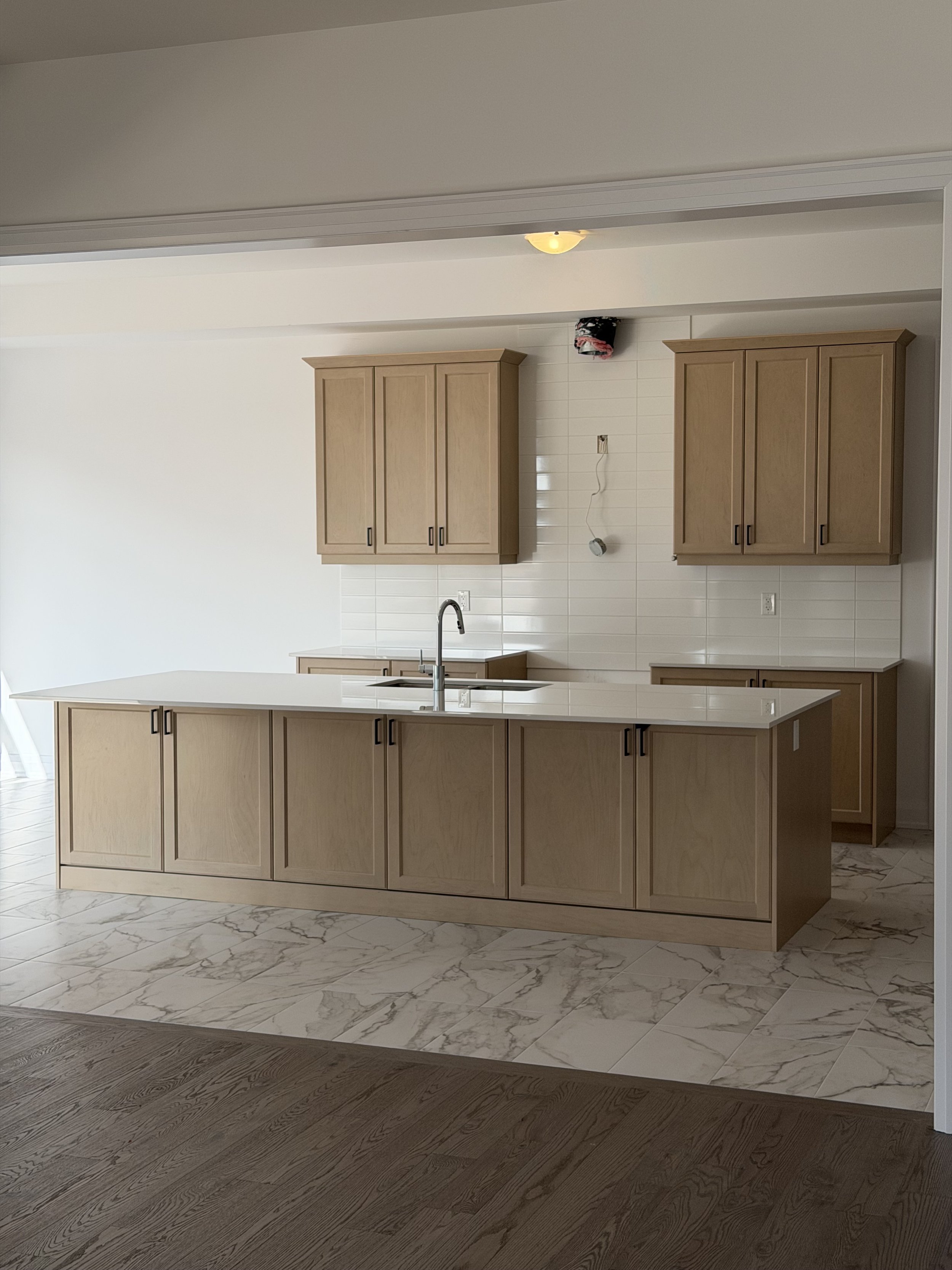 Modern kitchen with beige cabinets, white countertops, marble flooring, tiled wall, and a kitchen sink with a faucet.