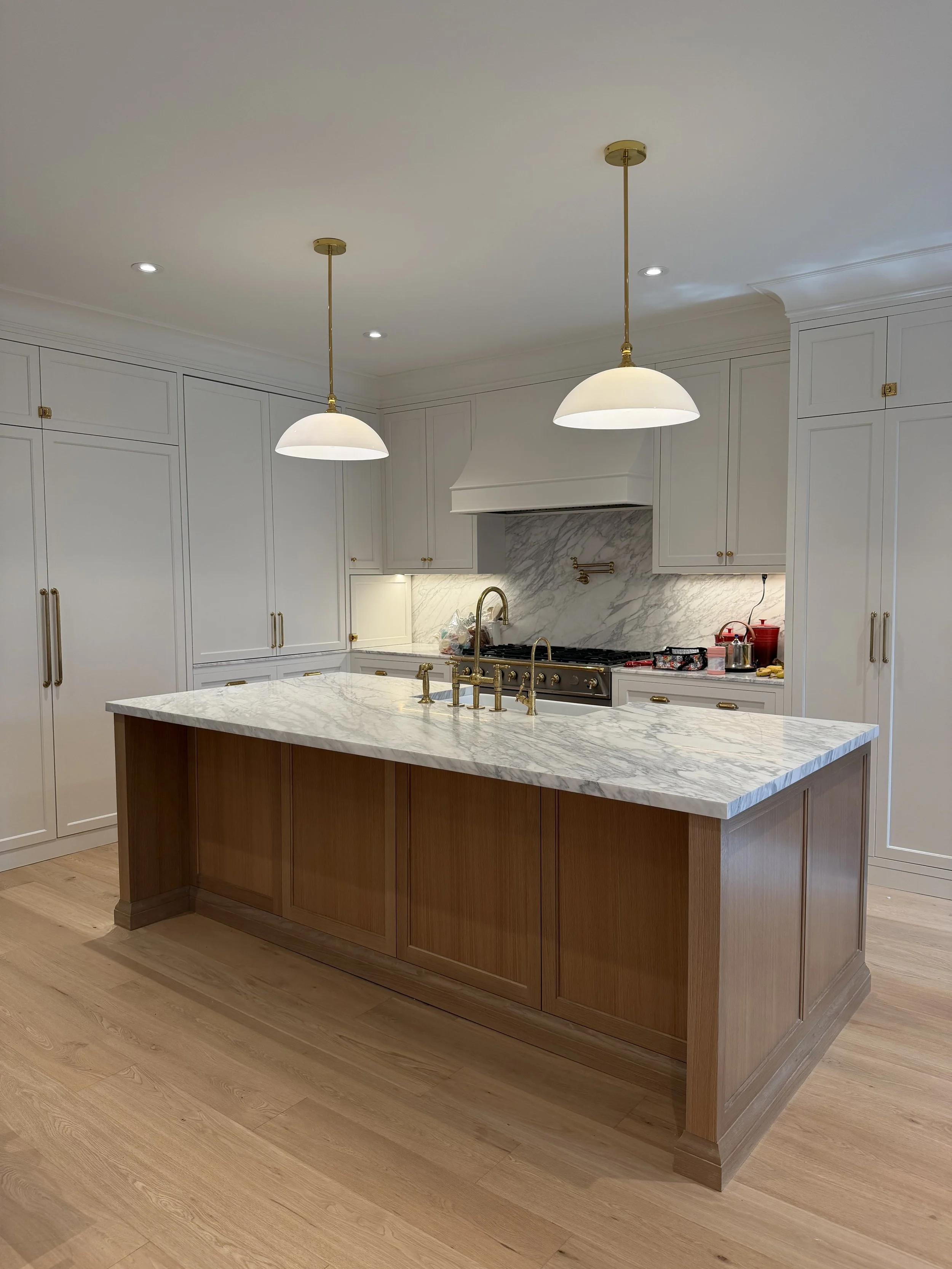 Modern kitchen with white cabinets, a marble backsplash, a marble countertop island with brass fixtures, and two white pendant lights hanging from the ceiling.