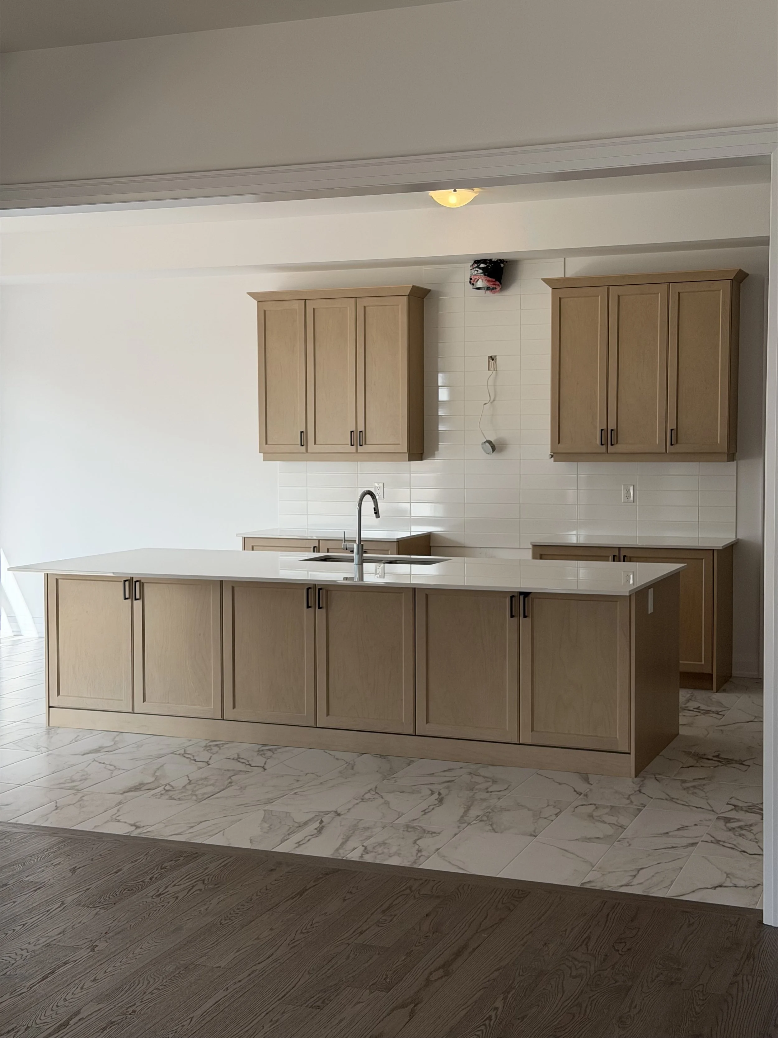 Newly installed kitchen with light wood cabinets, white marble floors, and a kitchen island with a built-in sink.