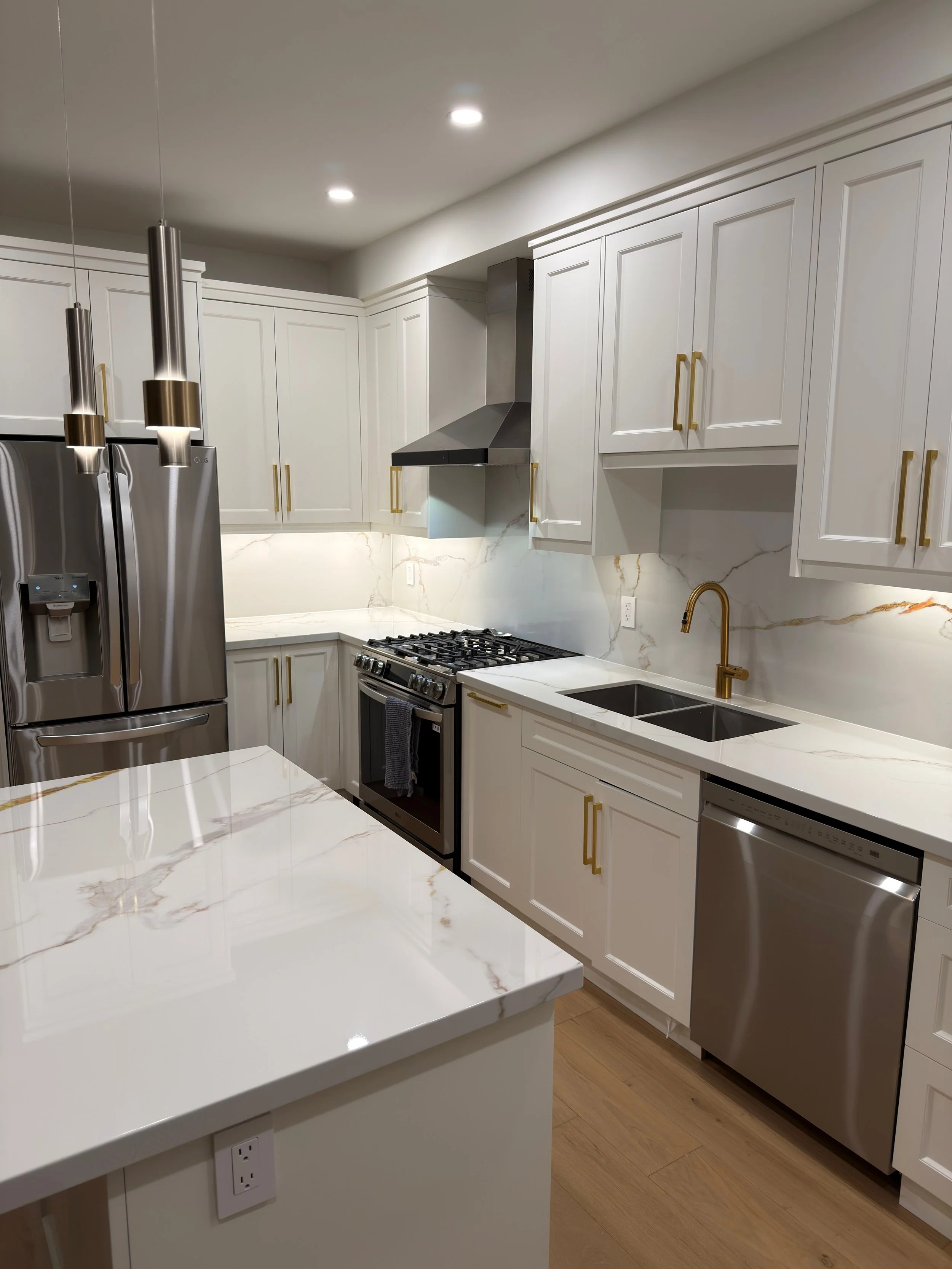 Modern kitchen with white cabinets, marble backsplash, stainless steel appliances, gold handles, and a gold faucet.