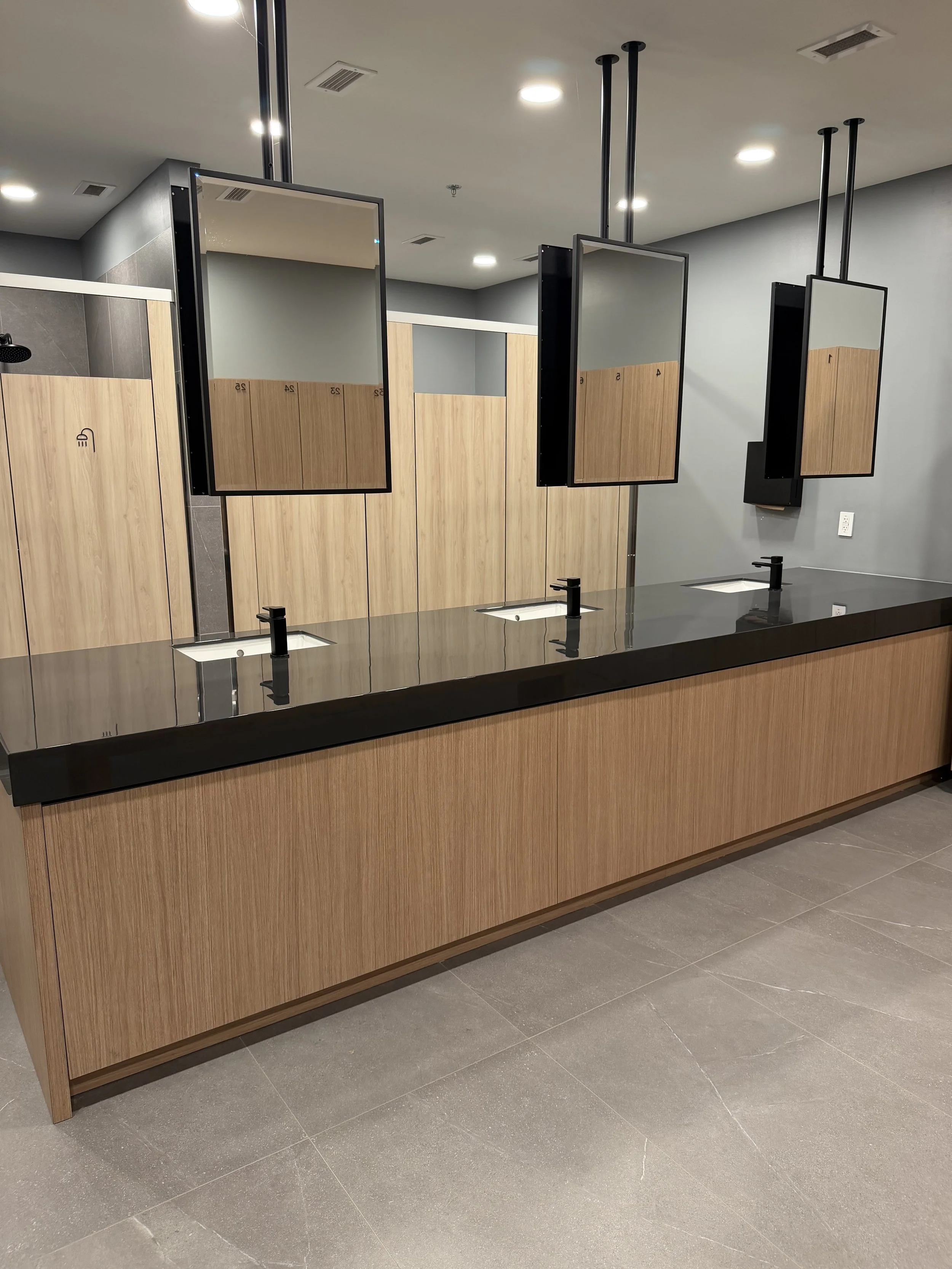 Public restroom sinks with black faucets, wooden paneling, mirrors, and partitioned stalls in the background.