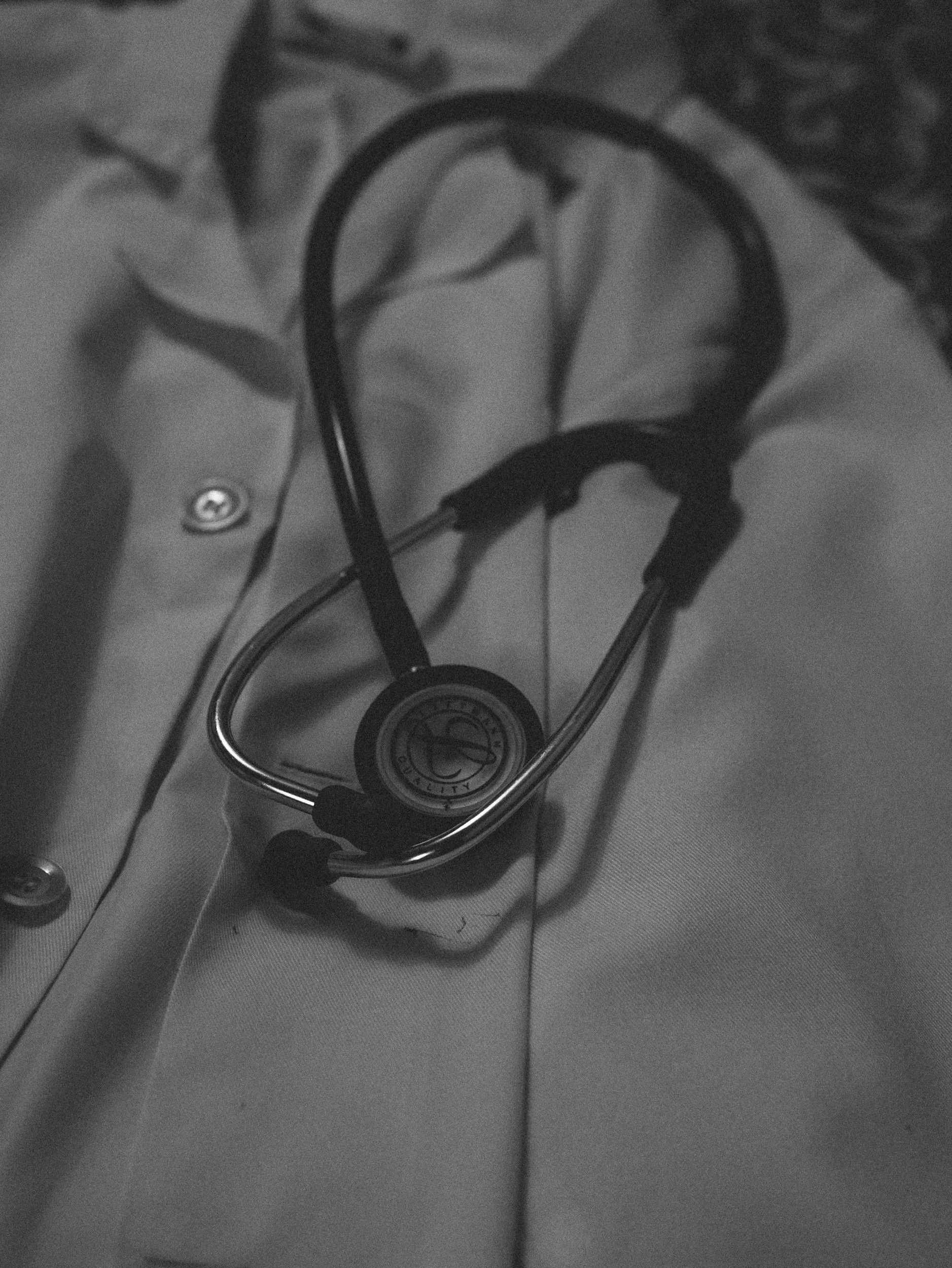 A stethoscope resting on a white medical coat. The stethoscope has a round chest piece and black tubing, placed on the chest pocket of the coat.