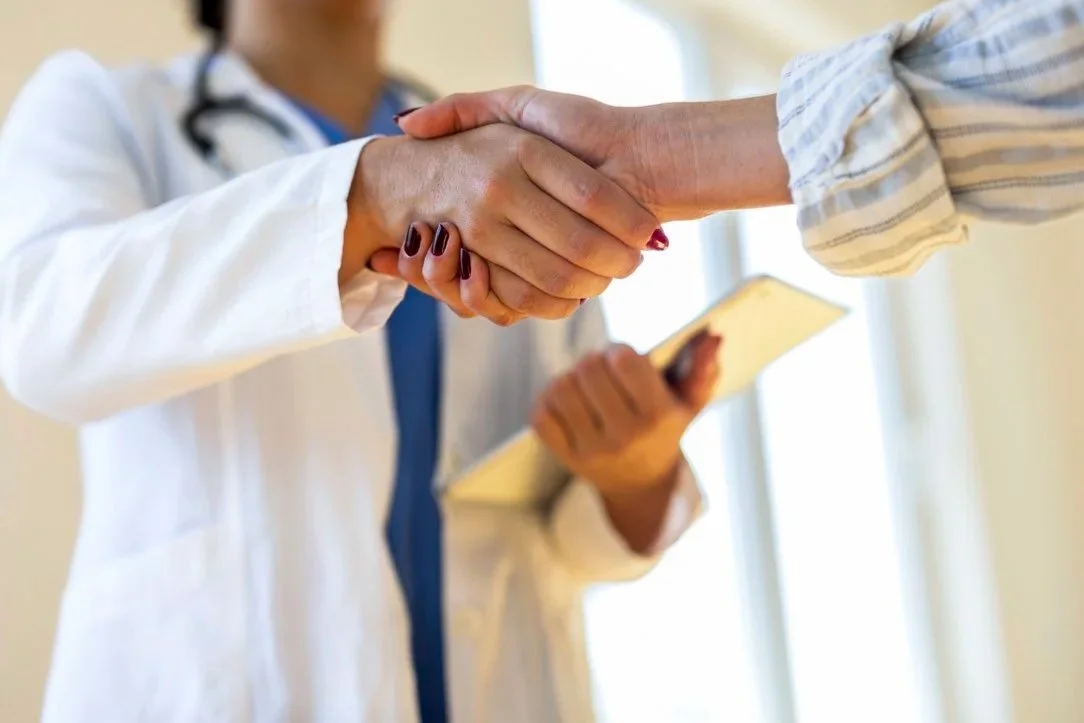 A healthcare professional in a white coat shaking hands with a patient.