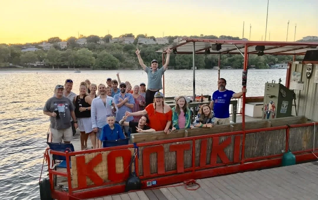 Group of people on a boat docked by a river at sunset.
