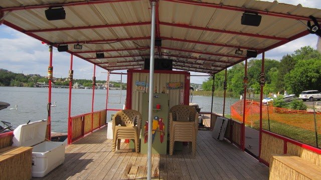View of a covered boat deck with chairs, a small table, and a safe, overlooking a body of water surrounded by trees.