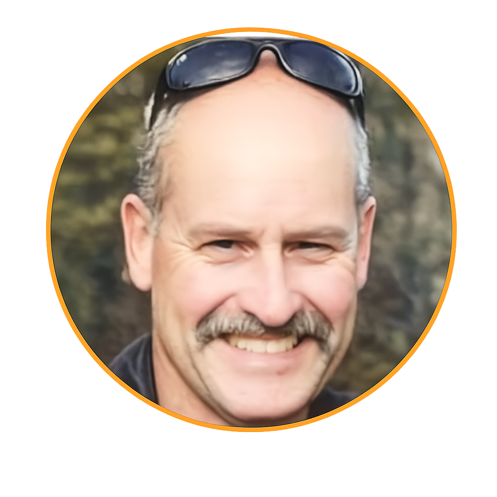 Close-up of a smiling middle-aged man with sunglasses on his head, curly gray hair, and a mustache, outdoors with a blurred natural background.