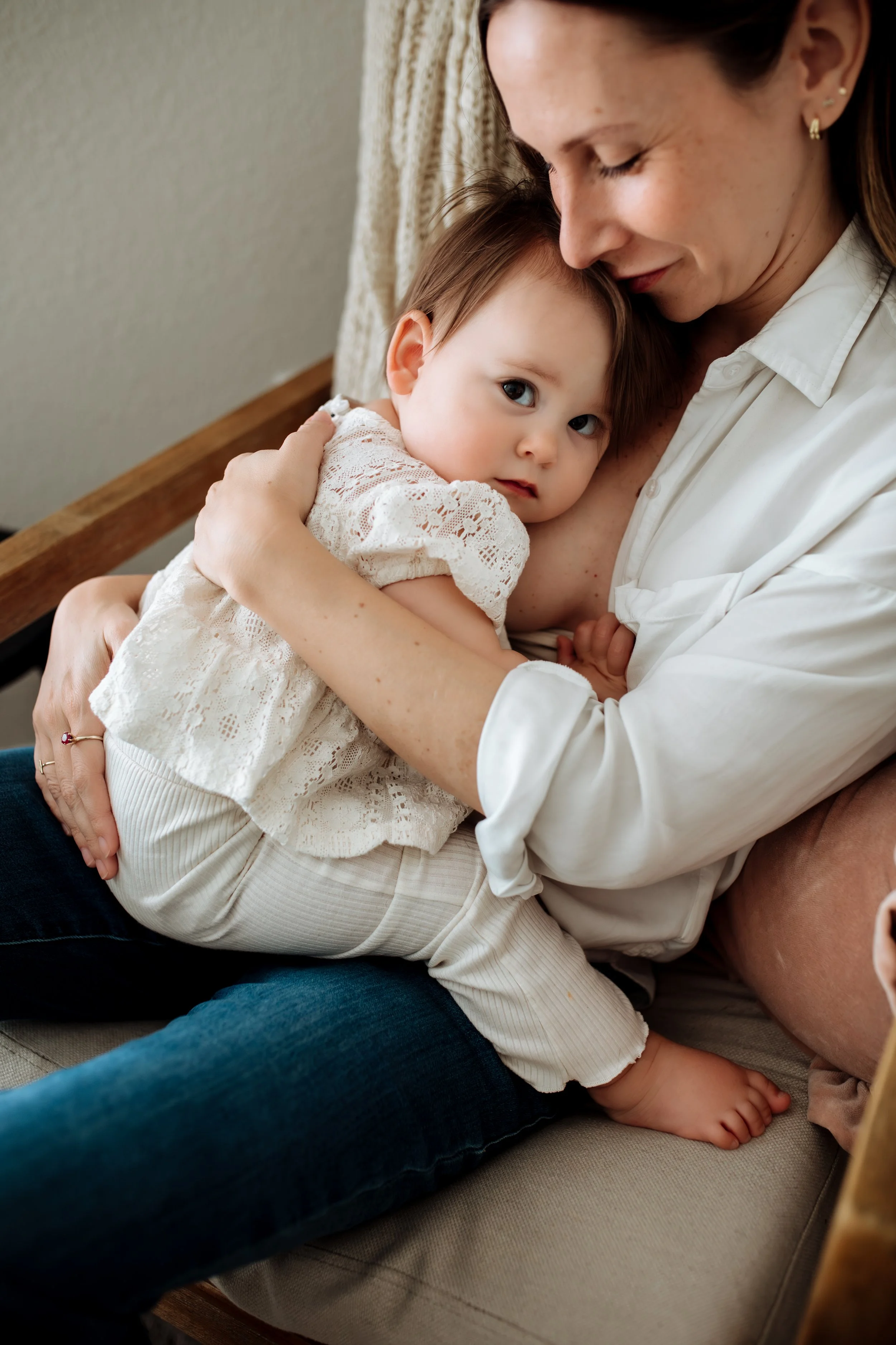 A woman is cuddling a young girl, resting her forehead on the child's head as they sit on a couch.