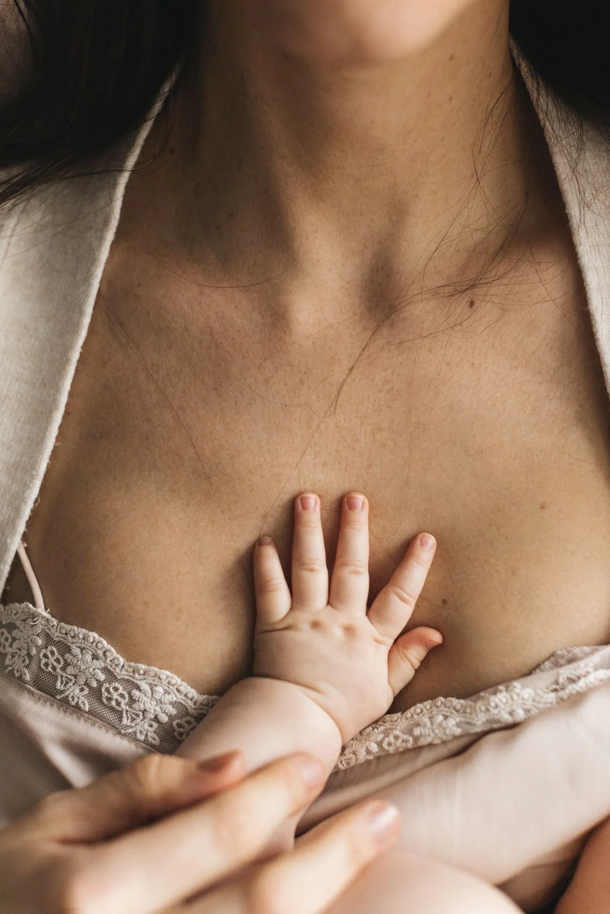 A close-up of a child's hand placed on an adult woman's chest area, showing part of her neck and neckline of a white top with lace trim.