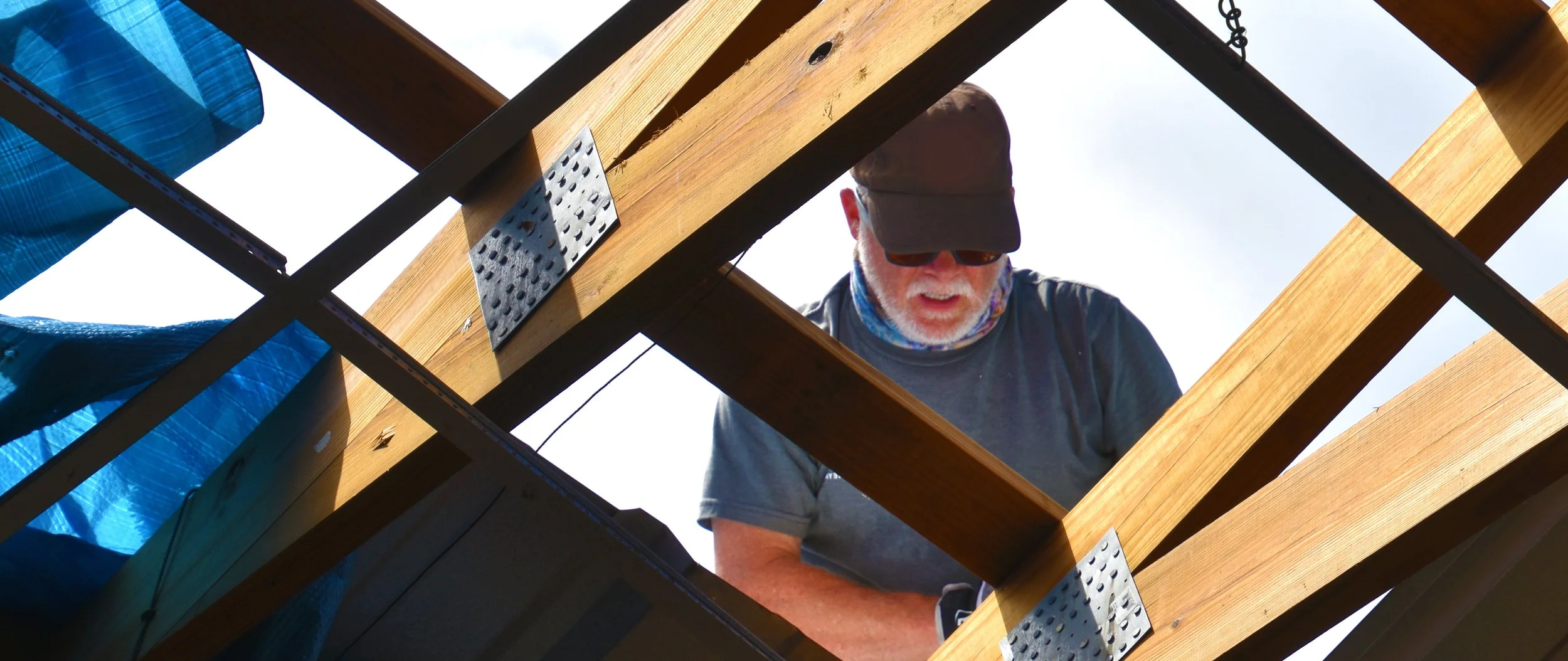 A man in hat and sunglasses repairing a roof in New Orleans after Hurricane Katrinah and debris along the shoreline during sunset.