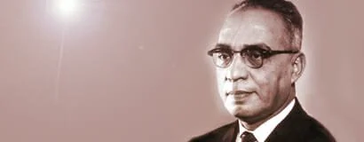 A sepia-toned portrait of a man with short hair, wearing glasses, a white shirt, and a dark suit.