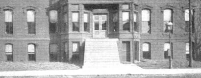 A large brick apartment building with a staircase leading to the entrance, multiple windows, and a brick facade.