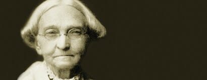 Black and white portrait of an elderly woman with glasses and short, wavy hair.