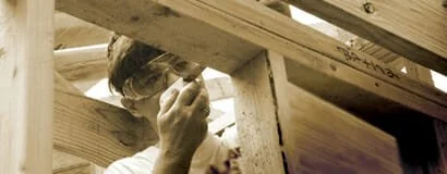 A person peeking through a small opening in a wooden structure.