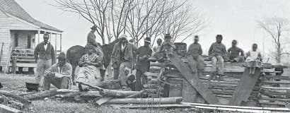 Group of people working outdoors with lumber and saws, possibly building a structure, in front of a house.