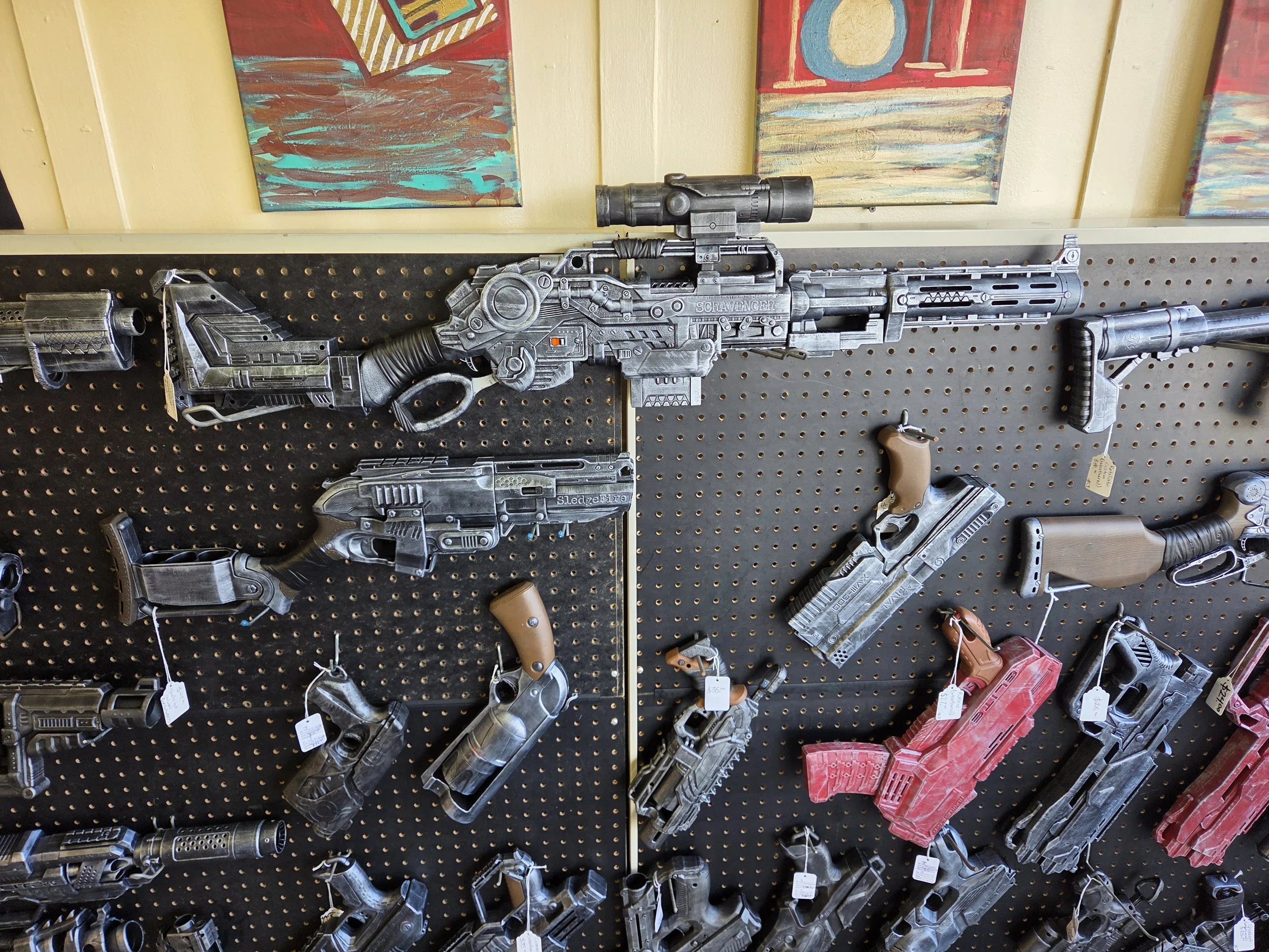 A peg board displaying custom painted Nerf guns in a variety of sizes and styles