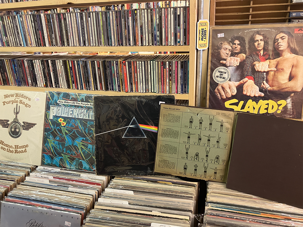 A shelves with rows of CDs and vinyl records, featuring Pink Floyd Dark Side of the Moon, New Riders of the Purple Sage Home, Home, on the Road, and Slade Slayed? albums, and many more.