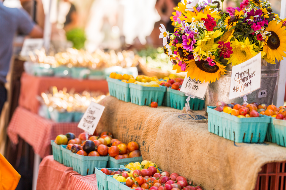 A display of colorful fruits, vegetables, and flowers in a farmer's market setting