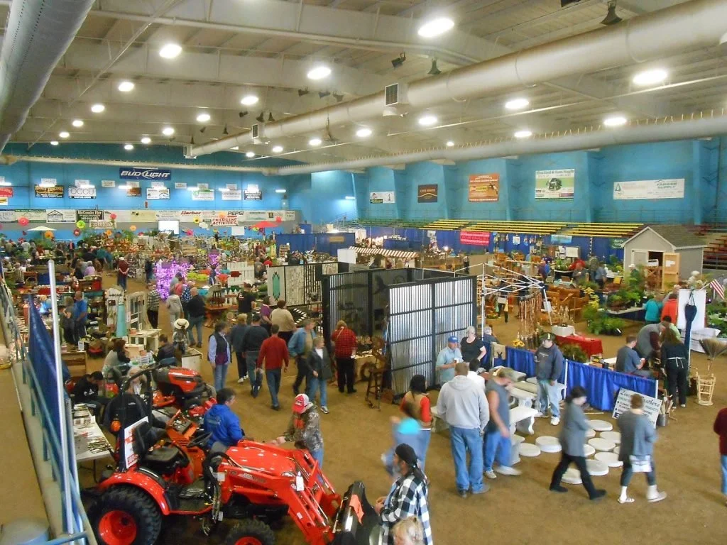 People moving through an expo featuring plants, garden equipment, tractors, and garden accessories.