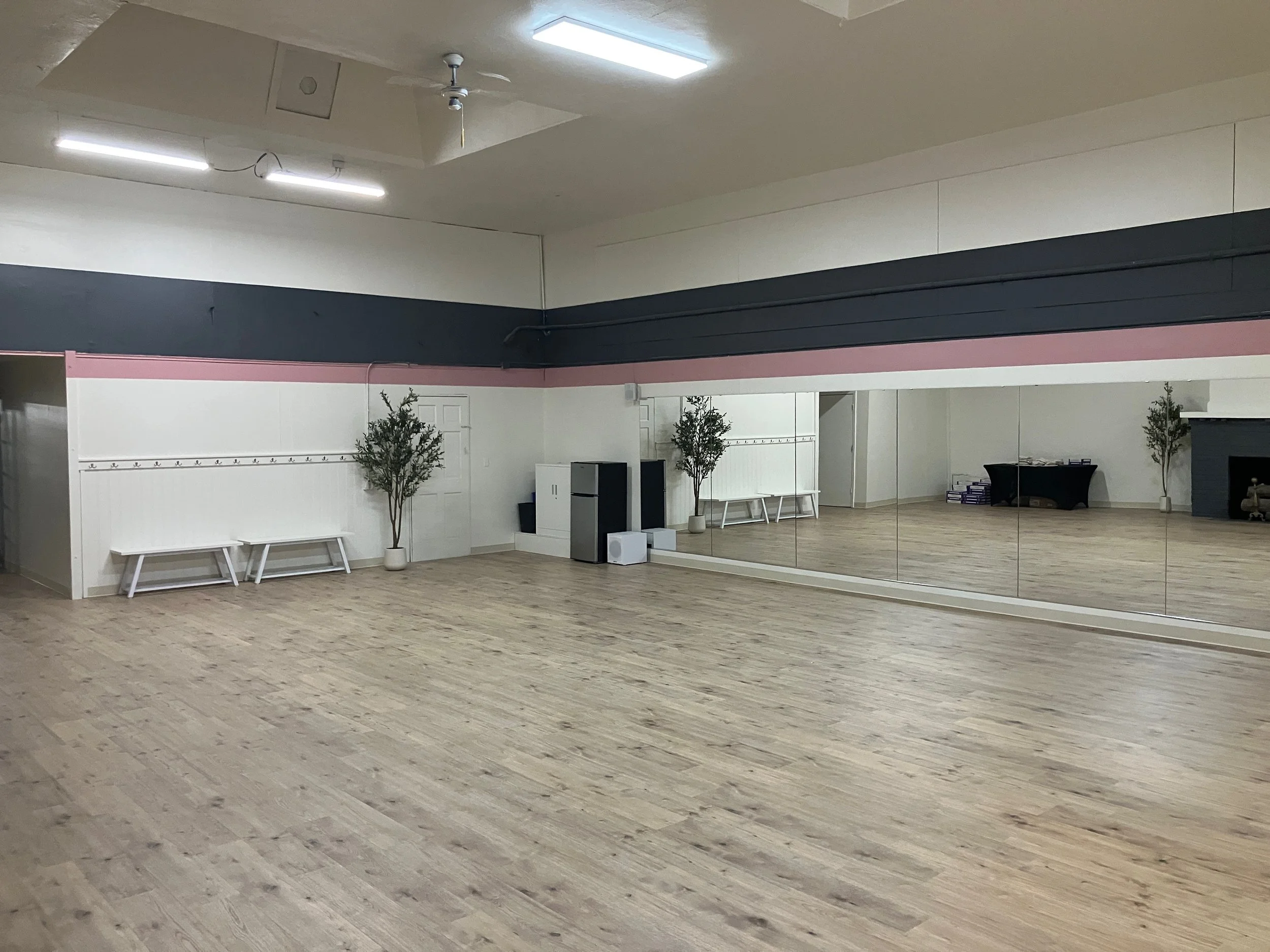 An empty dance or exercise studio with wood flooring and large mirror wall.