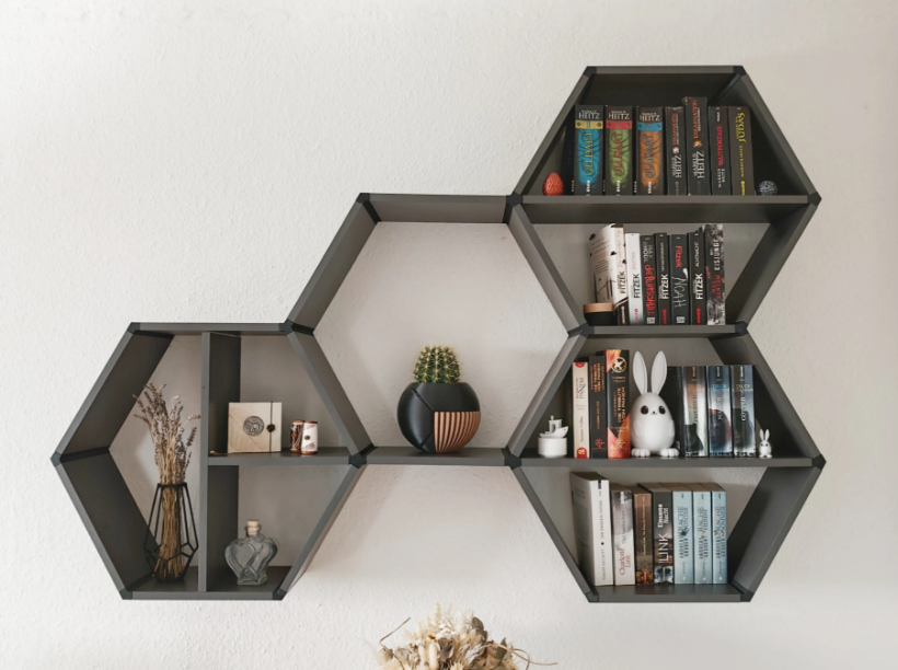 Decorative 3D printed hexagon shelves mounted on a wall with books, a small cactus, a rabbit-shaped figurine, books, and various decorative items.