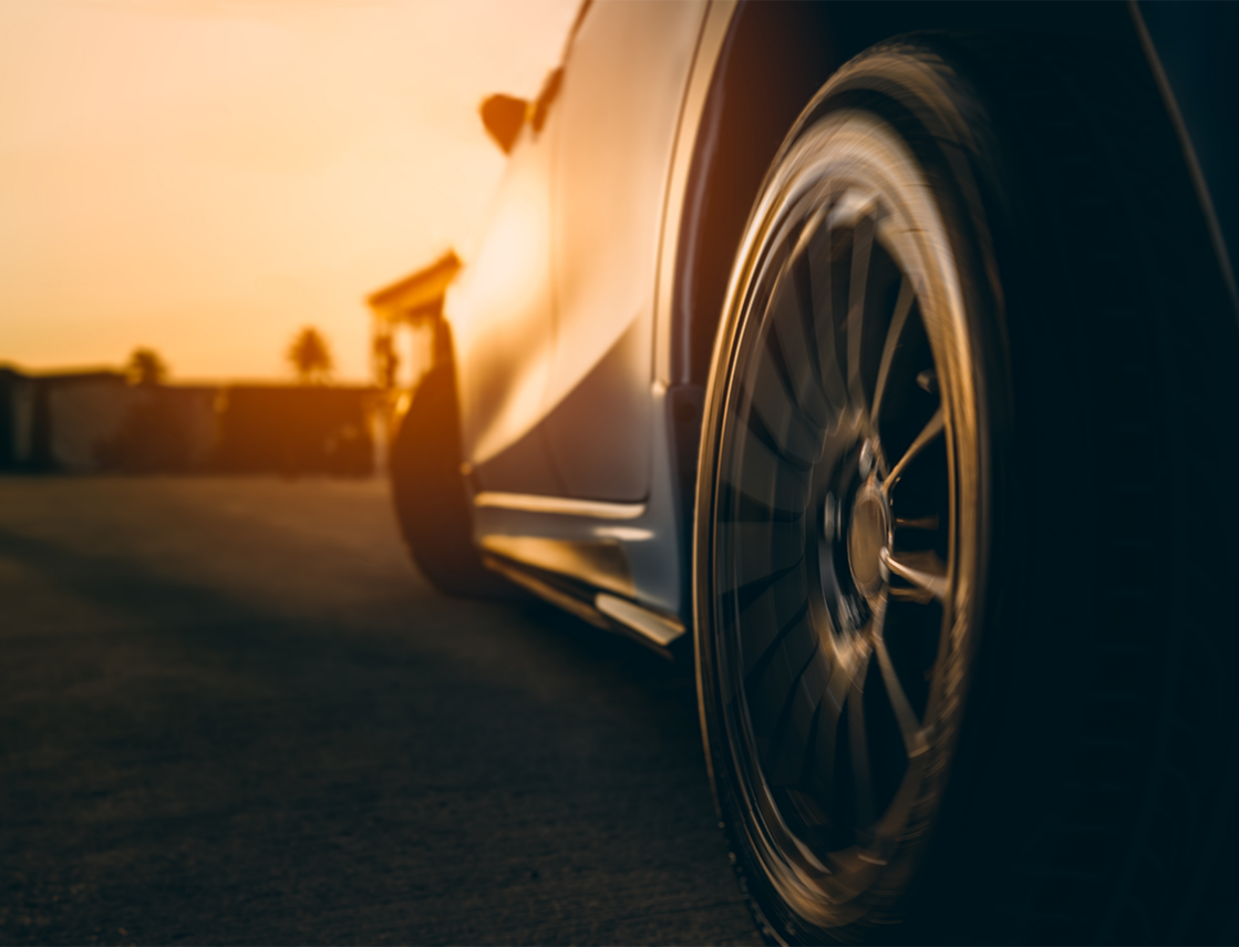 Close-up of a car wheel on a sports car, with the setting sun in the background.