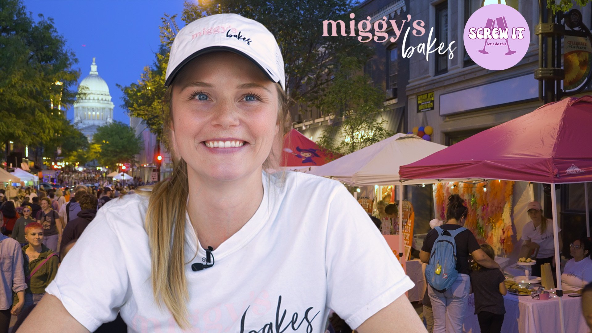 A woman smiling at an outdoor fair with vendor booths and a crowd of people, and the U.S. Capitol building in the background, during evening time.