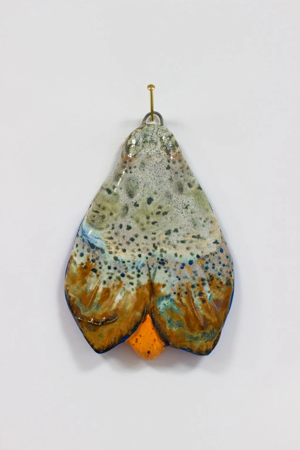 Keraaminen taideteos, joka muistuttaa kärpästä tai muuta hyönteistä, roikkuu itsestään naulassa.