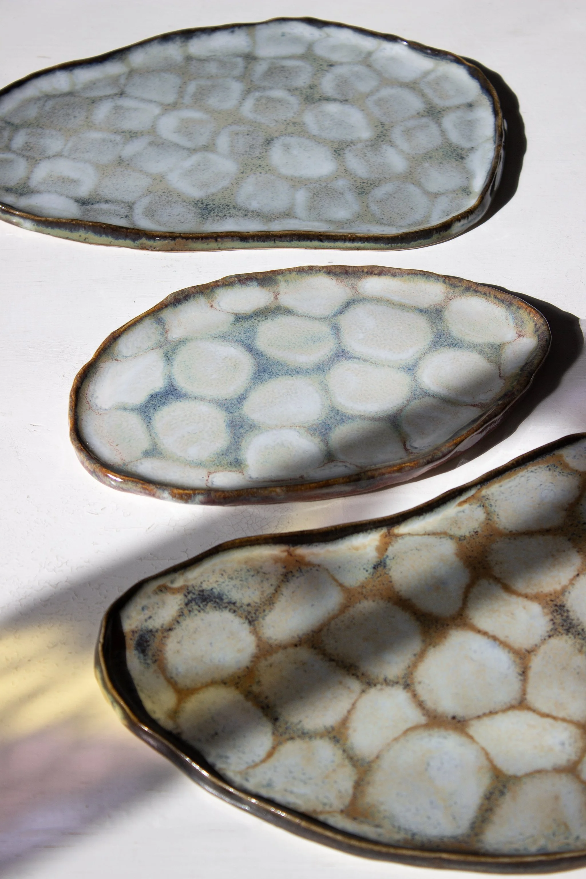 Kolme keramiikkalautasta, istutettu yhteiseen muotoon, kuvattuna valossa, varjot osittain peittävät osia lautasista.