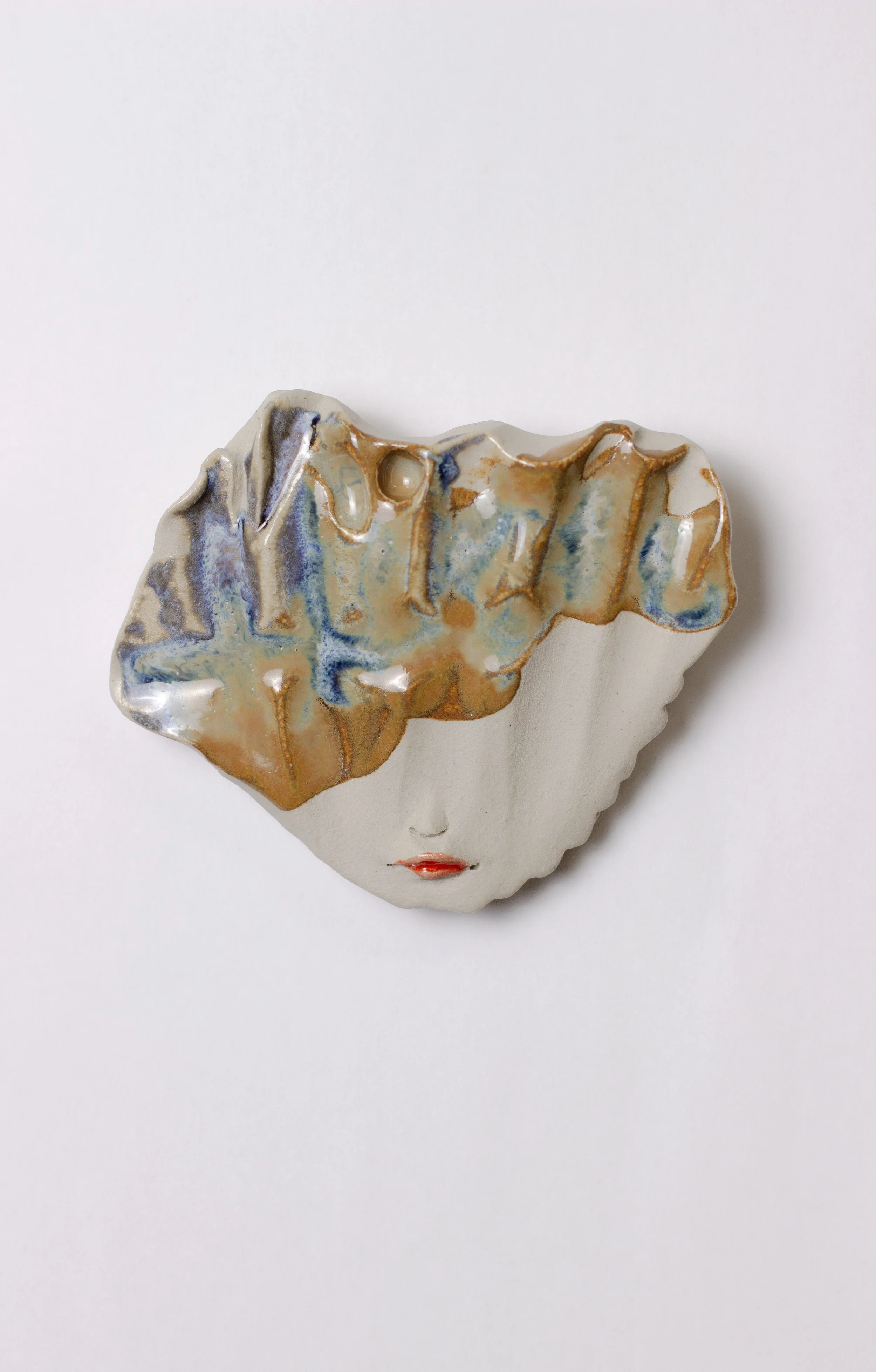 Kuvassa on taidemaalauksesta inspiroitu keramiikkateos, jossa on ihmisen kasvot ja abstrakti lasite, jossa on sinisiä, ruskeita ja kultahtavia sävyjä.