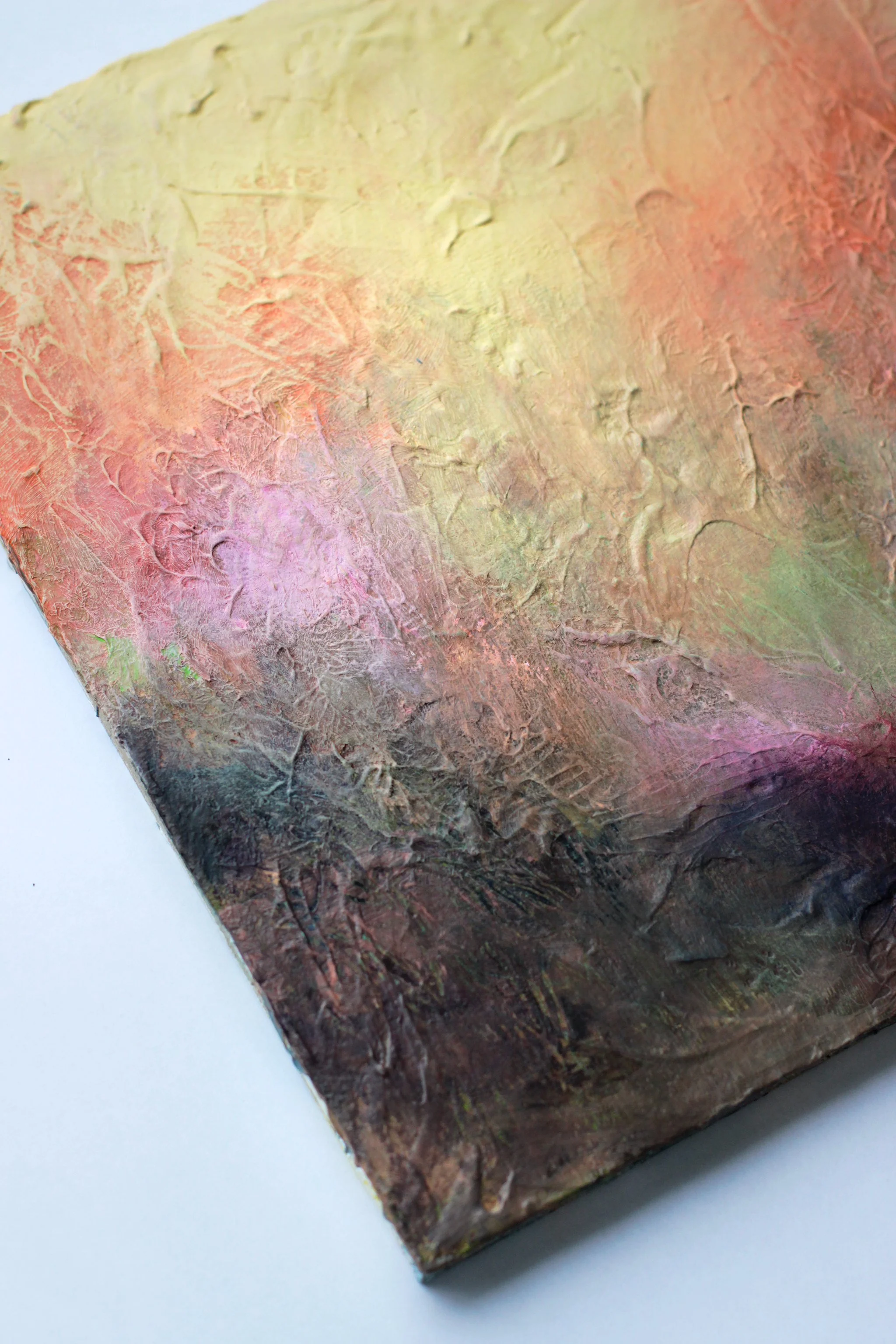 Kuva abstraktista maalauspinnasta, jossa on pehmeitä värejä kuten pinkki, keltainen, oranssi ja ruskea, ja tekstuureja.