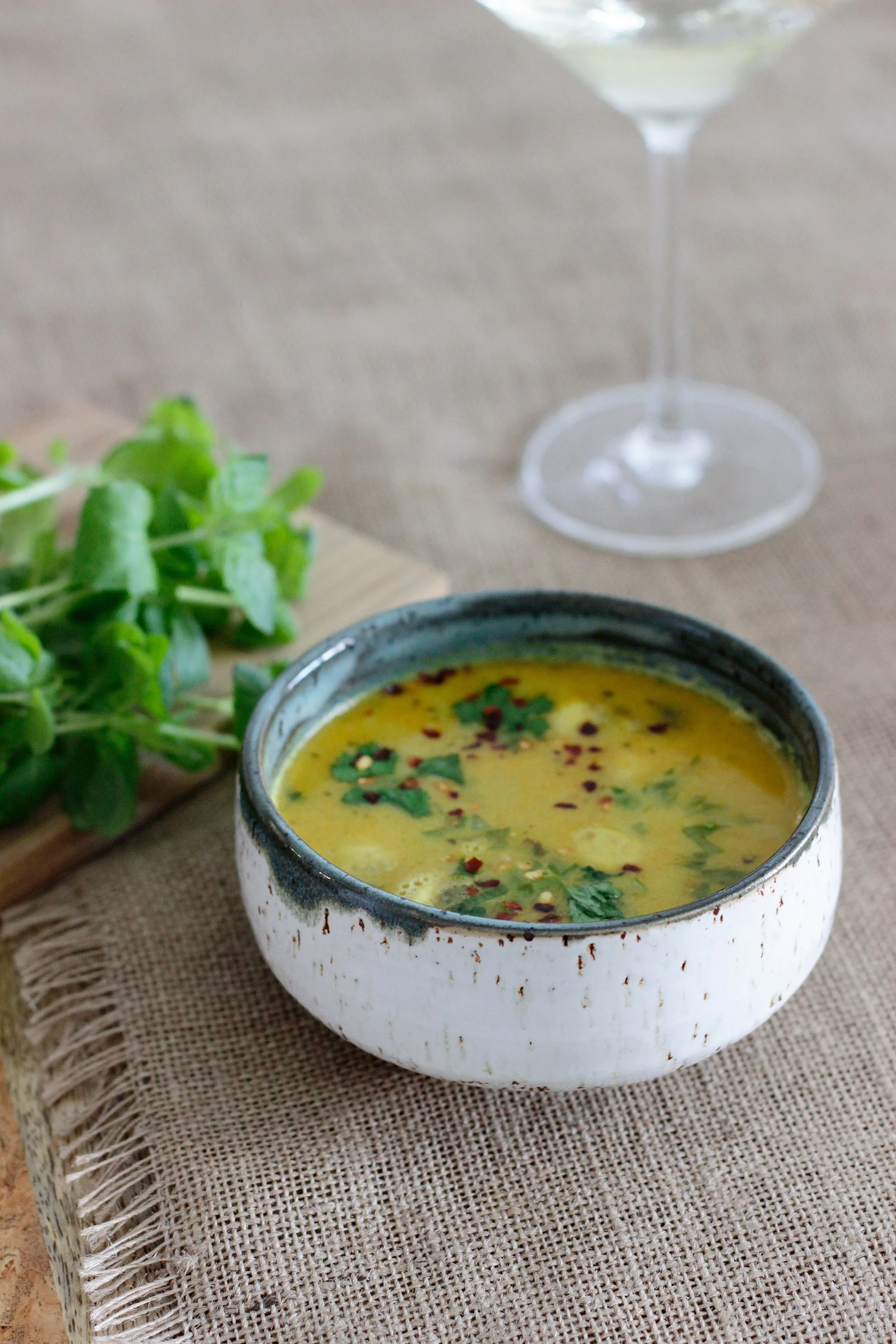 Kuvassa on kulho thai-keittoa, tuoreen yrtin koristelulla, vieressä vihreää salaattia ja  viinilasi