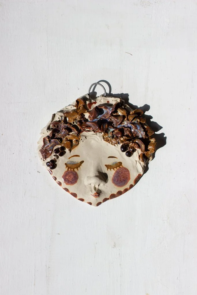 Käsinmaalattu seinäkaunotarmaski, jossa on suloinen kasvot, kiinnitetty valkoiseen taustaseinään.