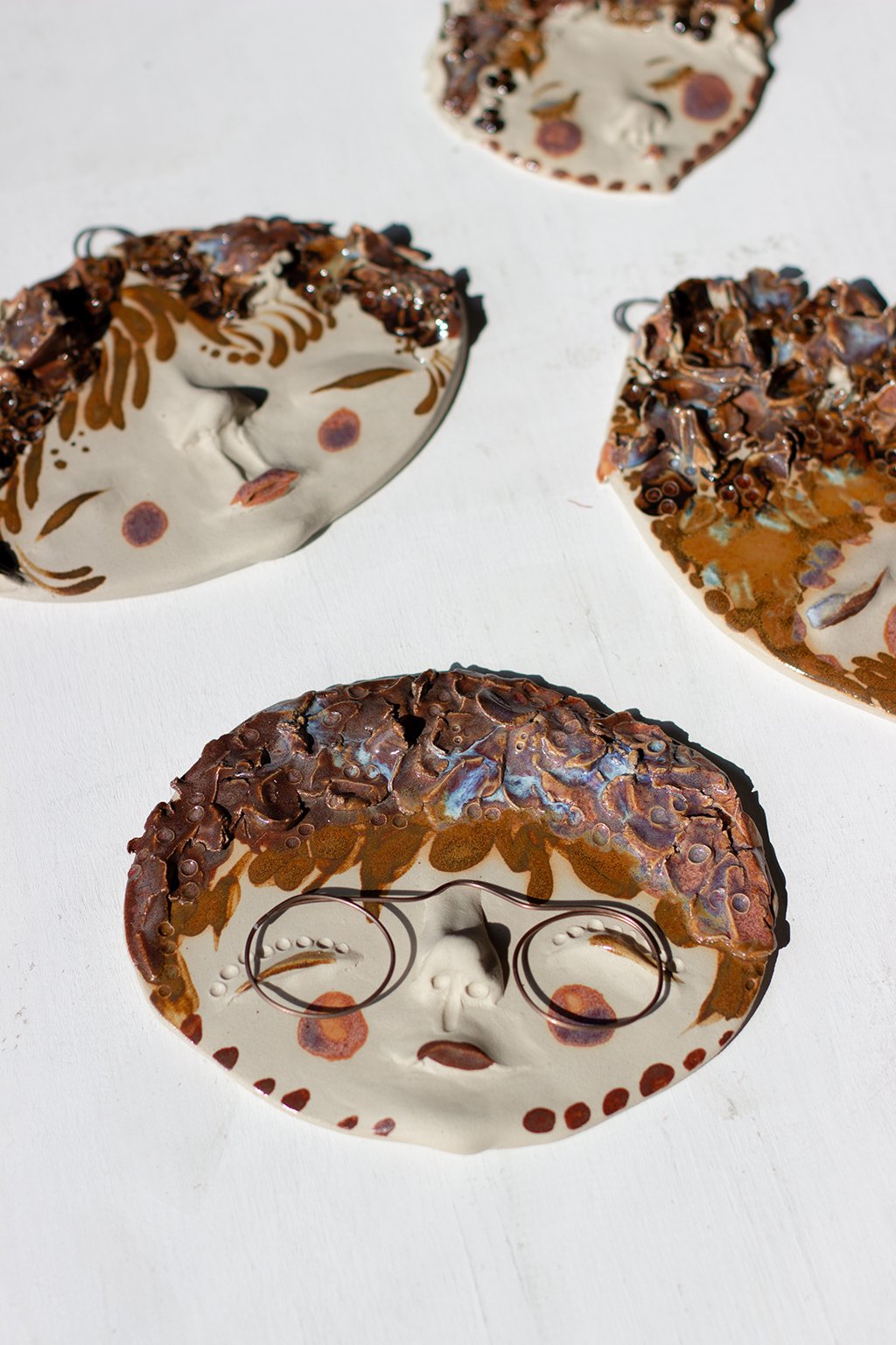 Neljä kasvoreliefiä, hahmojen hiukset päällystetty ruskealla lasitteella