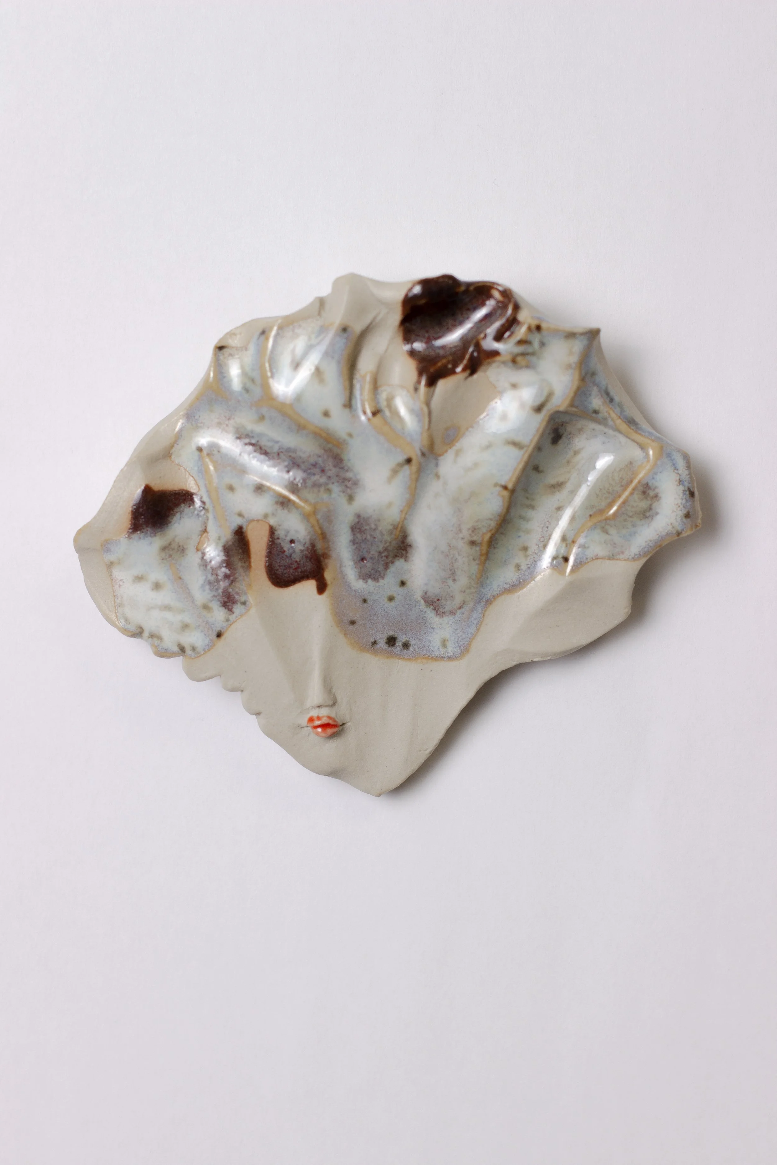 Koristetaideteos, jossa keramiikkaa, jossa ihmisen kasvot ja abstraktisia muotoja.