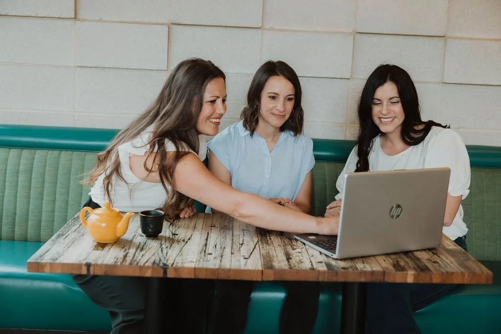 Erin and Keri consulting interior designer on business strategy, all three look at a laptop together while Erin Hildmann points at the screen